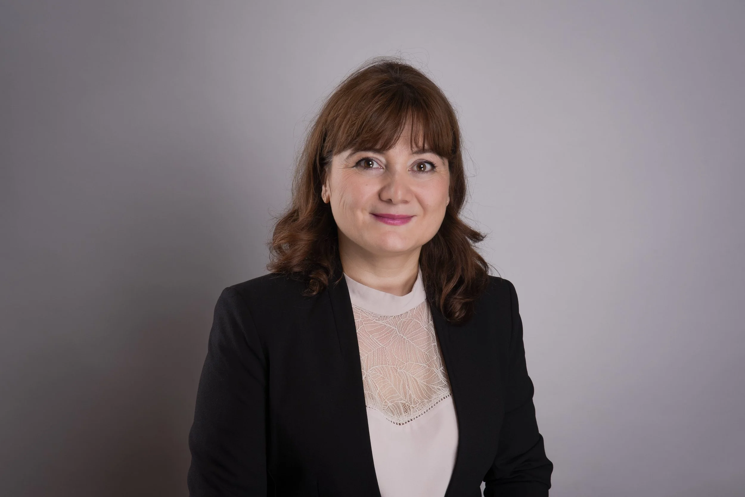 Porträt auf Lela, schwarze Jacke und weißes Top vor grauem Hintergrund.