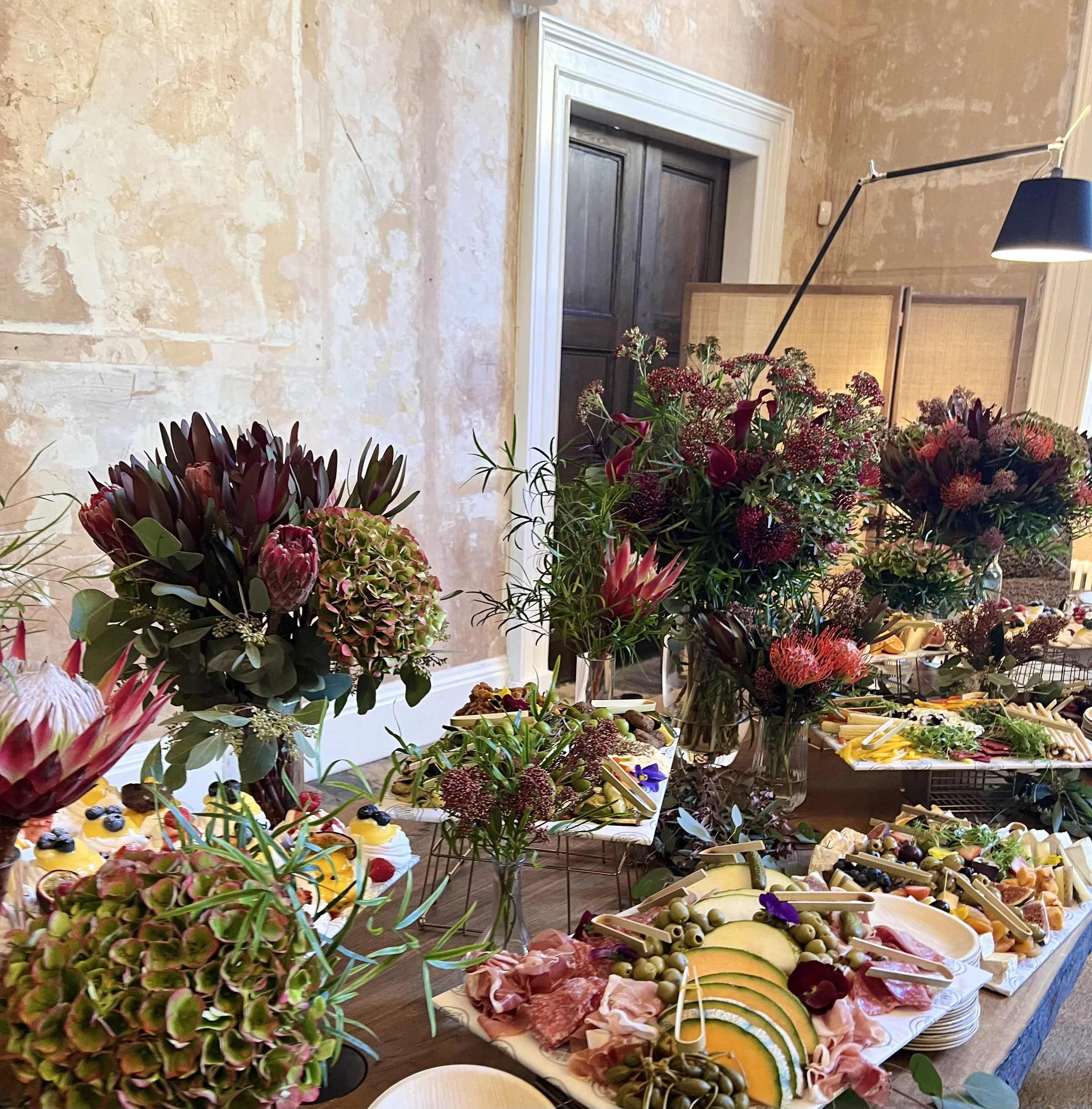 A BEAUTIFULLY STYLED GRAZING TABLE WITH CHEESES, CURED MEATS, FRESH FRUIT AND ELABORATE FLOWERS.