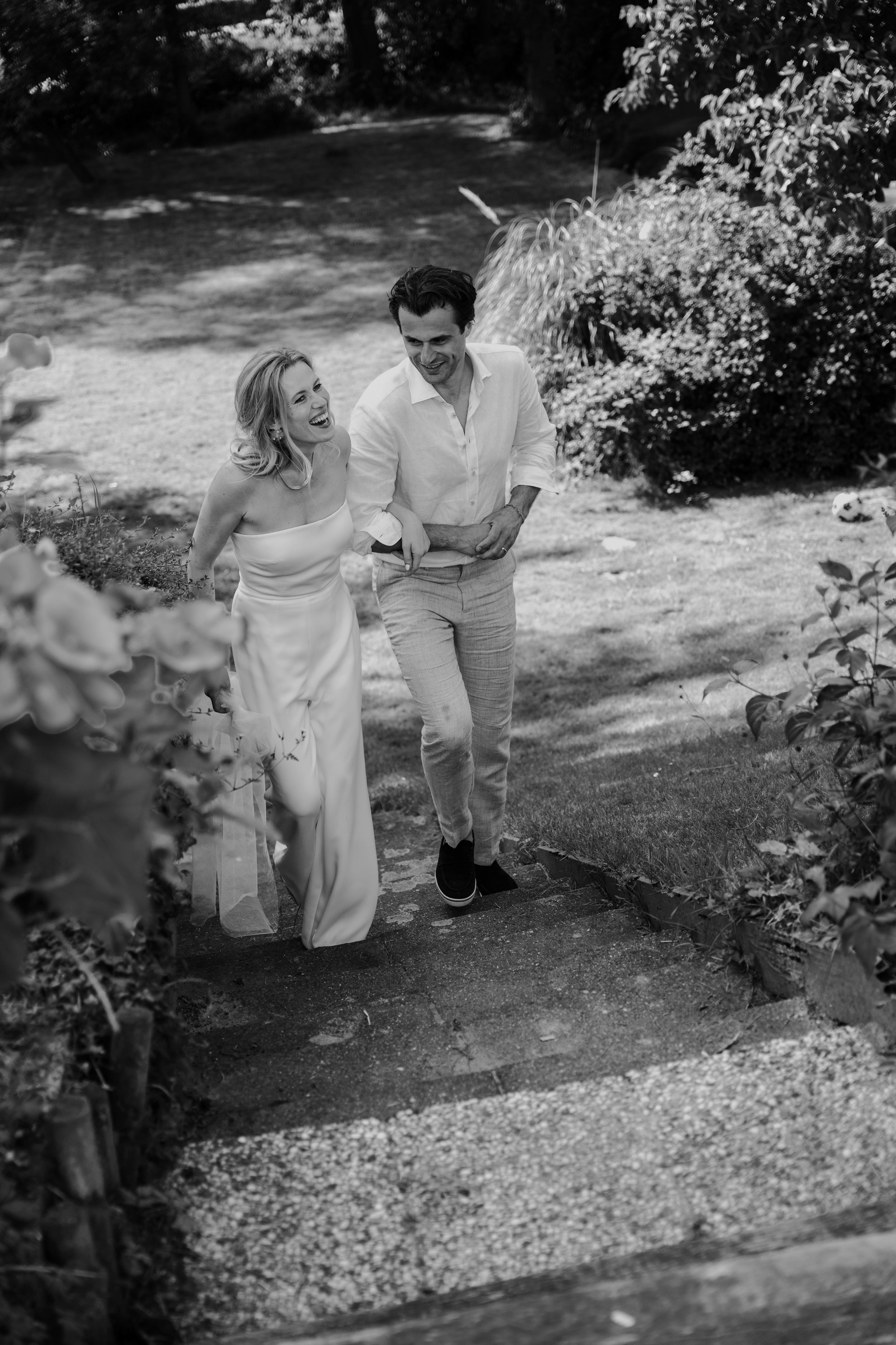 There are a man and a woman walking on a garden path, smiling and laughing, in black and white.