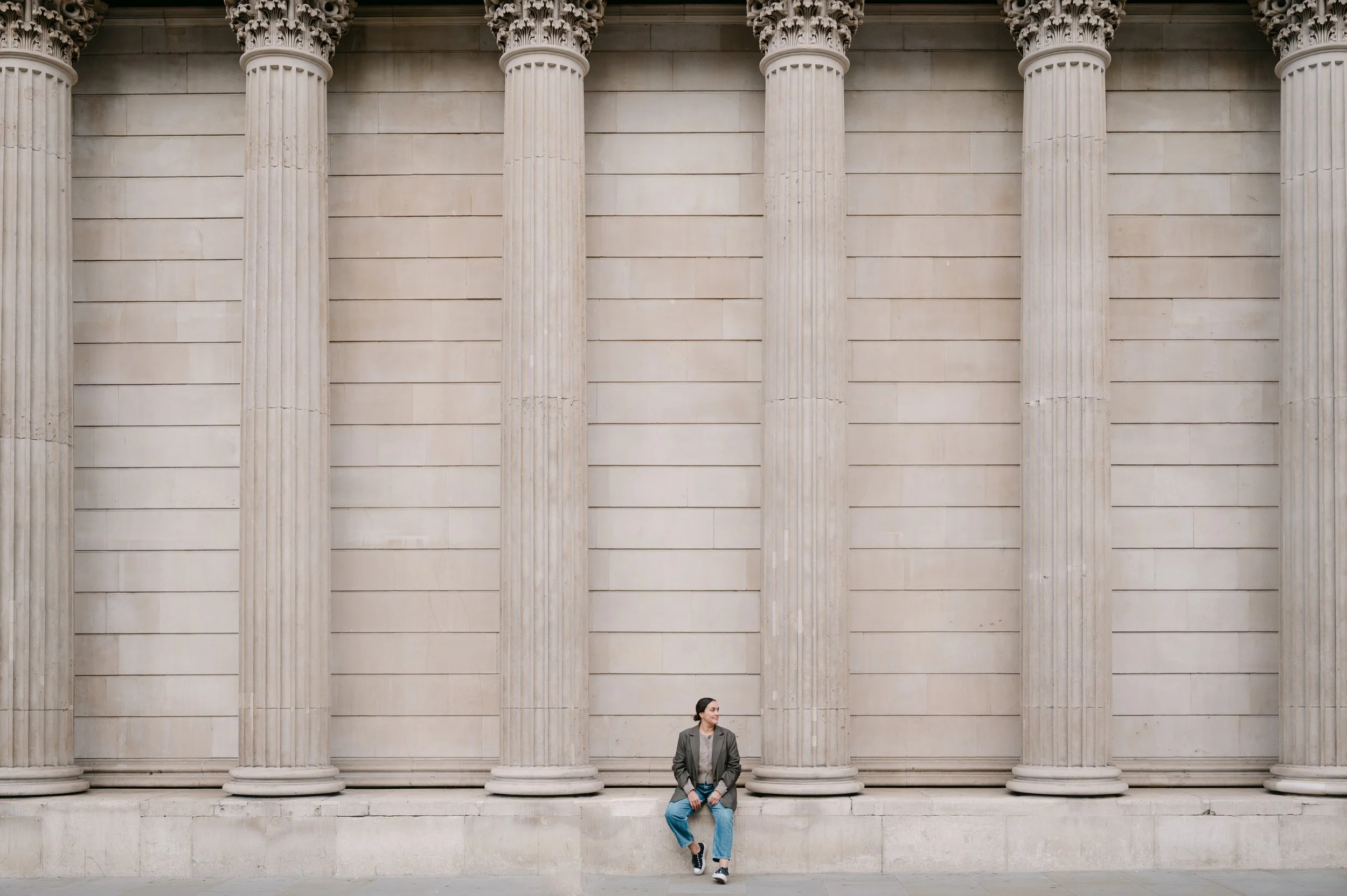 Vrouw zit op een rand voor een grote muur met Griekse zuilen.