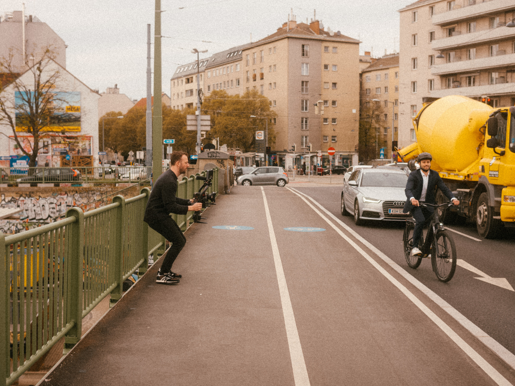 Ein Mann steht mit einer Videokamera auf einer Brücke und filmt einen Fahrradfahrer