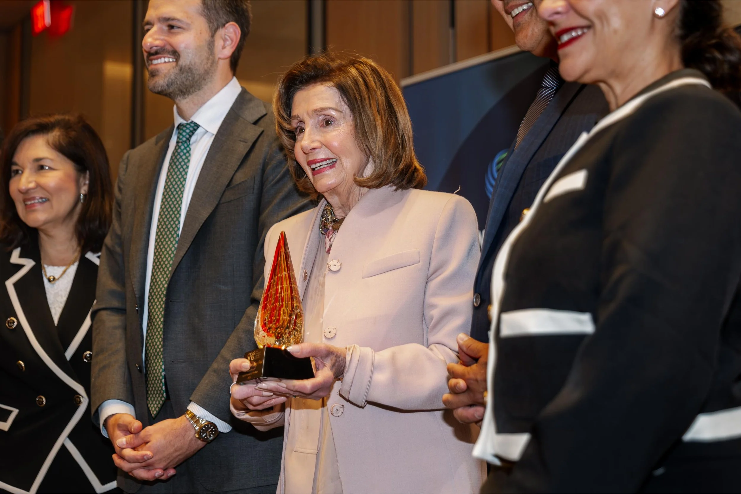 Woman in beige blazer holding an award, surrounded by four other professionally dressed individuals at an awards event.