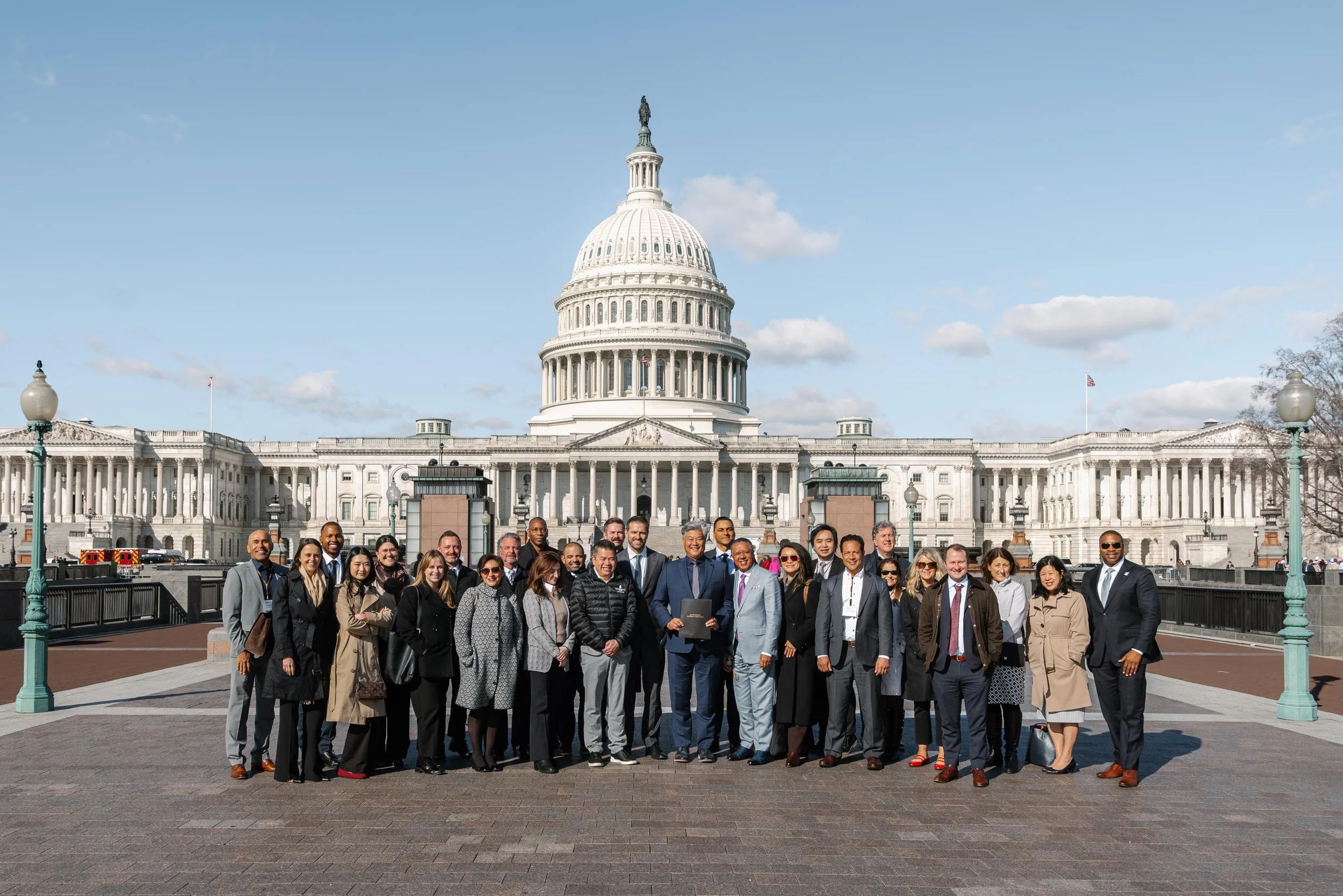 Group of diverse people standing in front of the U.S. Capitol building on a bright sunny day.