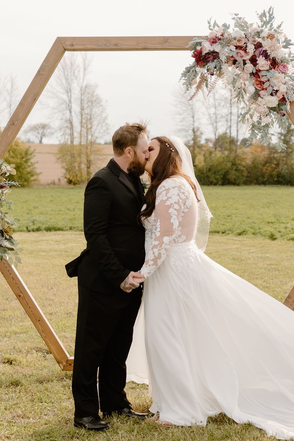 Couple kissing in front of hexagon wood wedding arch