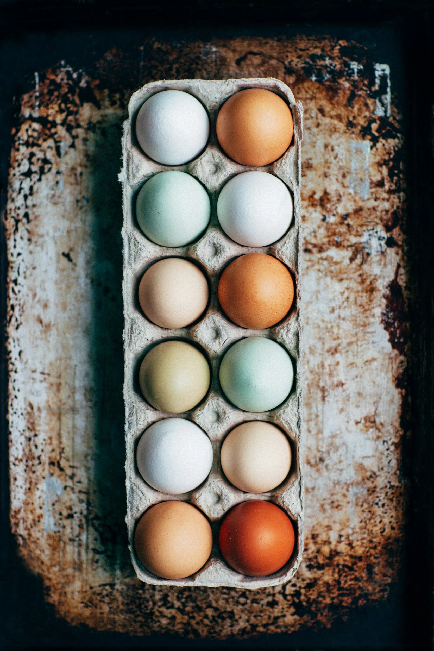 A carton of ten colorful eggs on a rustic, textured surface.