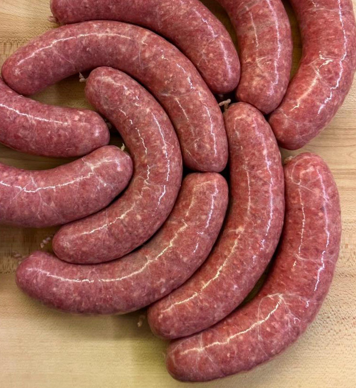 Raw sausages arranged in a spiral on a wooden surface.