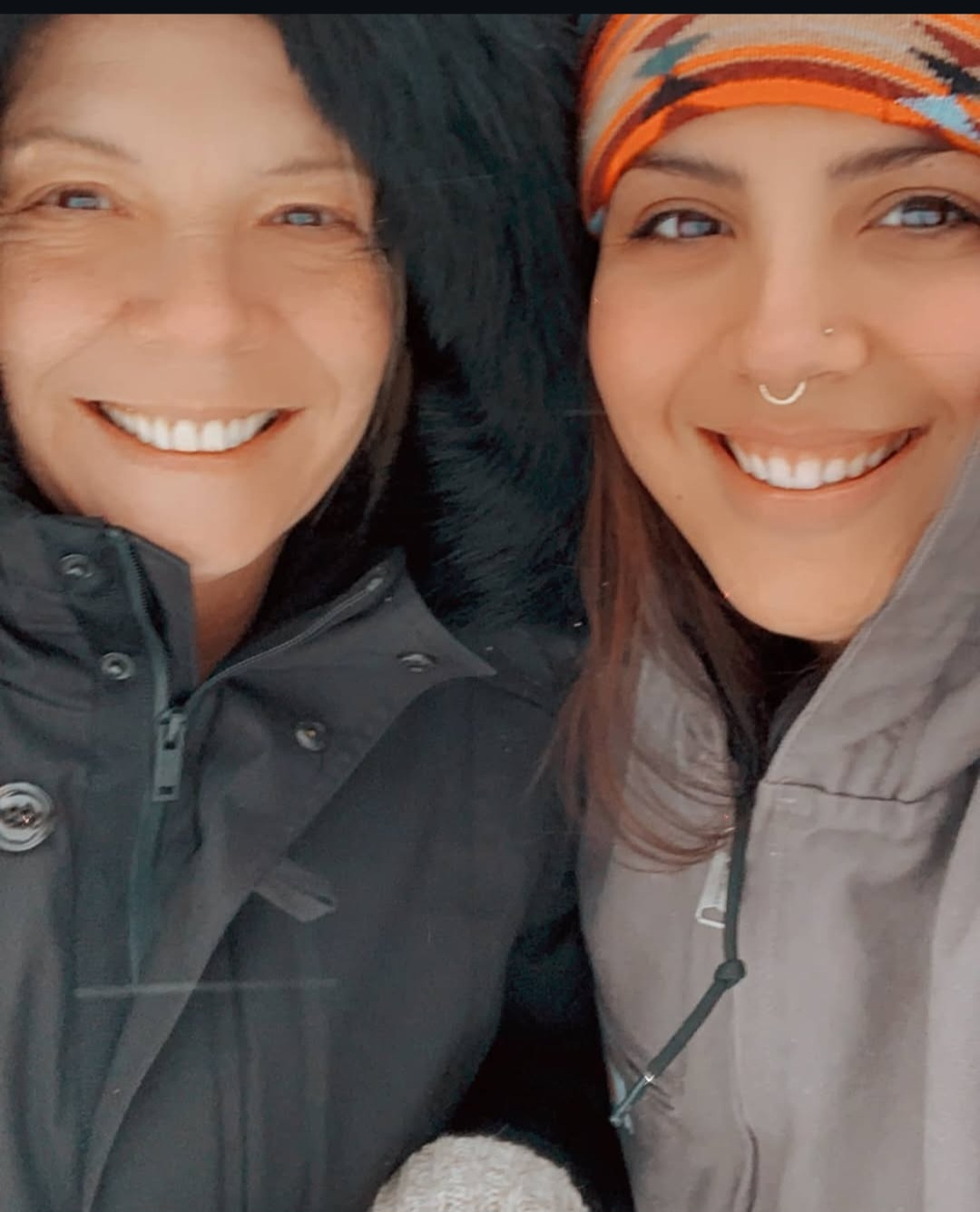 Two smiling women outdoors, wearing warm jackets and one with a colorful headscarf.