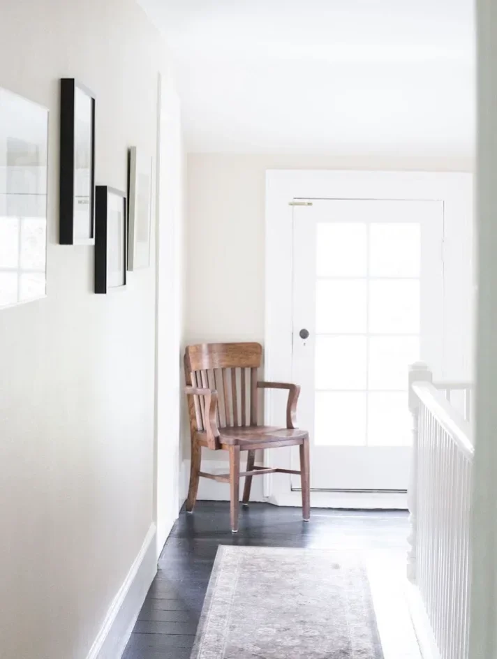 Narrow white hallway with a wooden chair, rug and glass door at the end