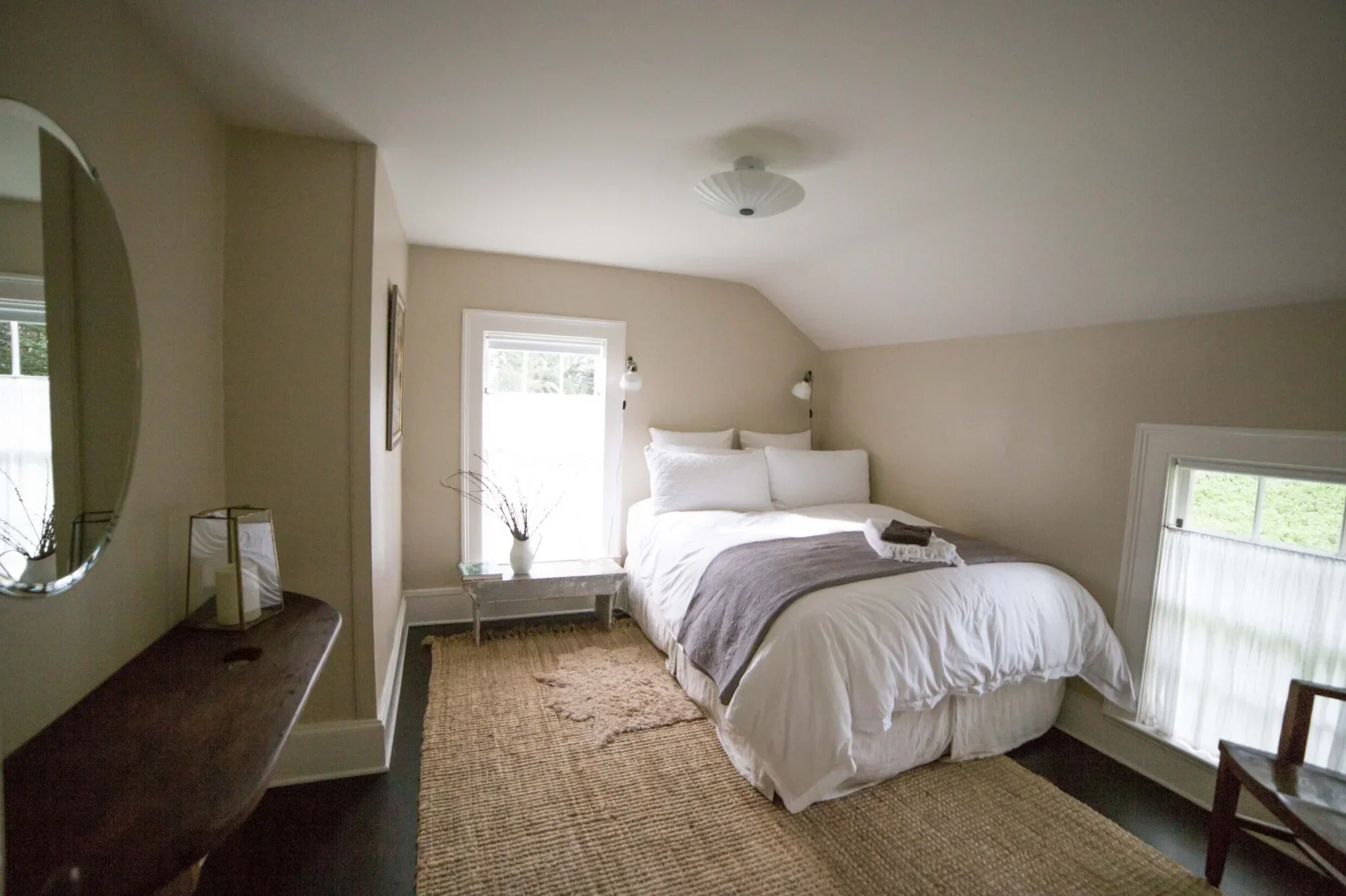 Bedroom with a round mirror, double bed and windows on two walls