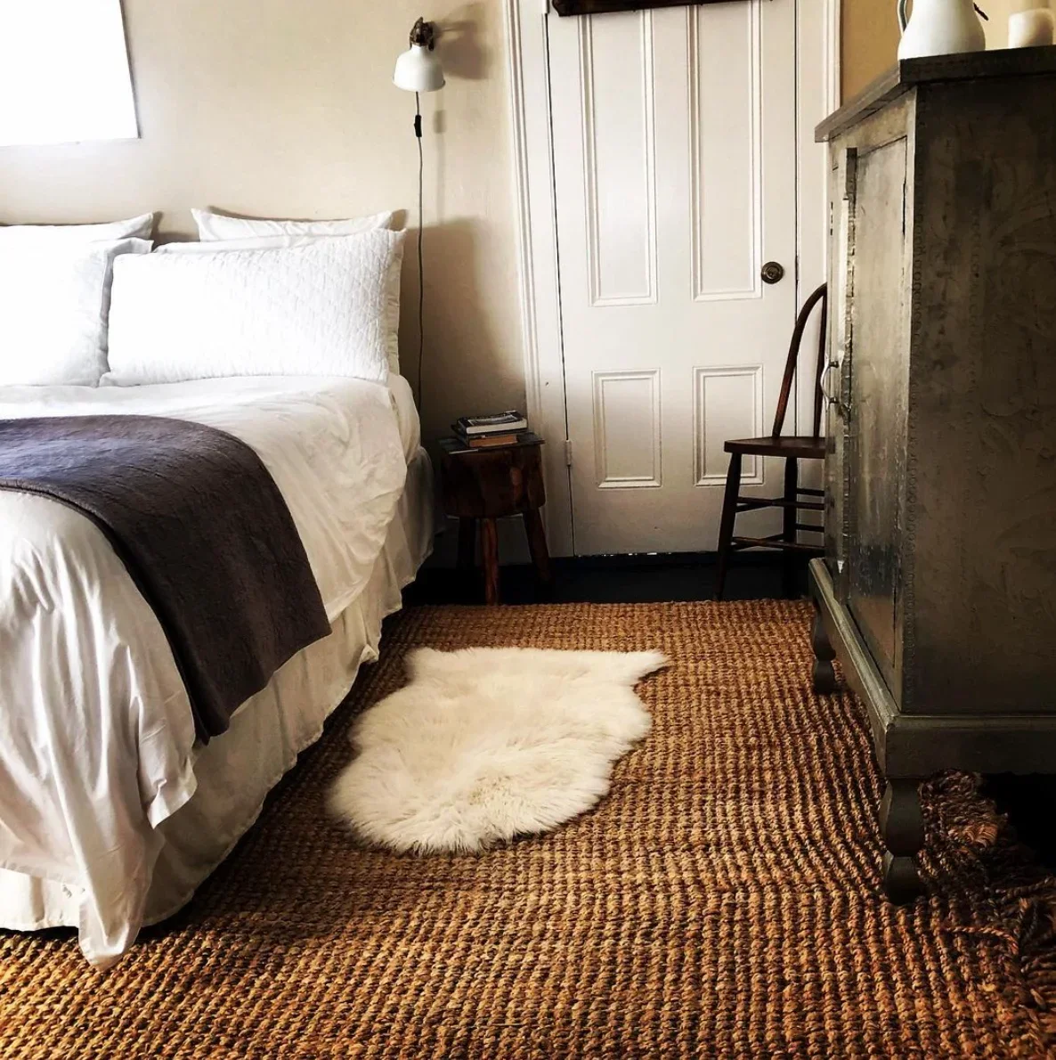 Bed with a gray throw and sheepskin rug beside a tall wooden wardrobe