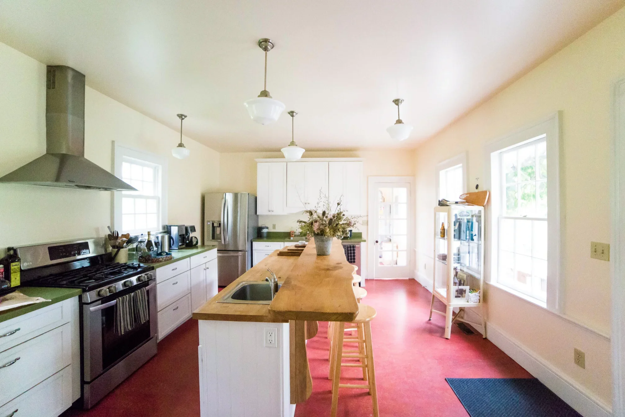Bright kitchen with a butcher-block island, stainless range and red floor