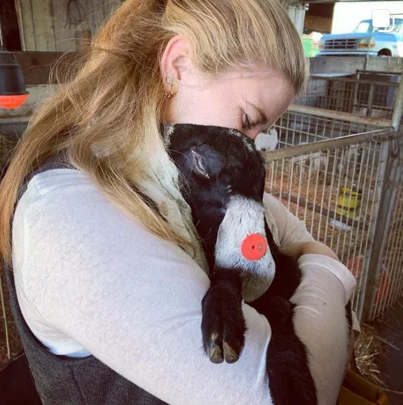 A woman cuddling a black baby goat in a barn