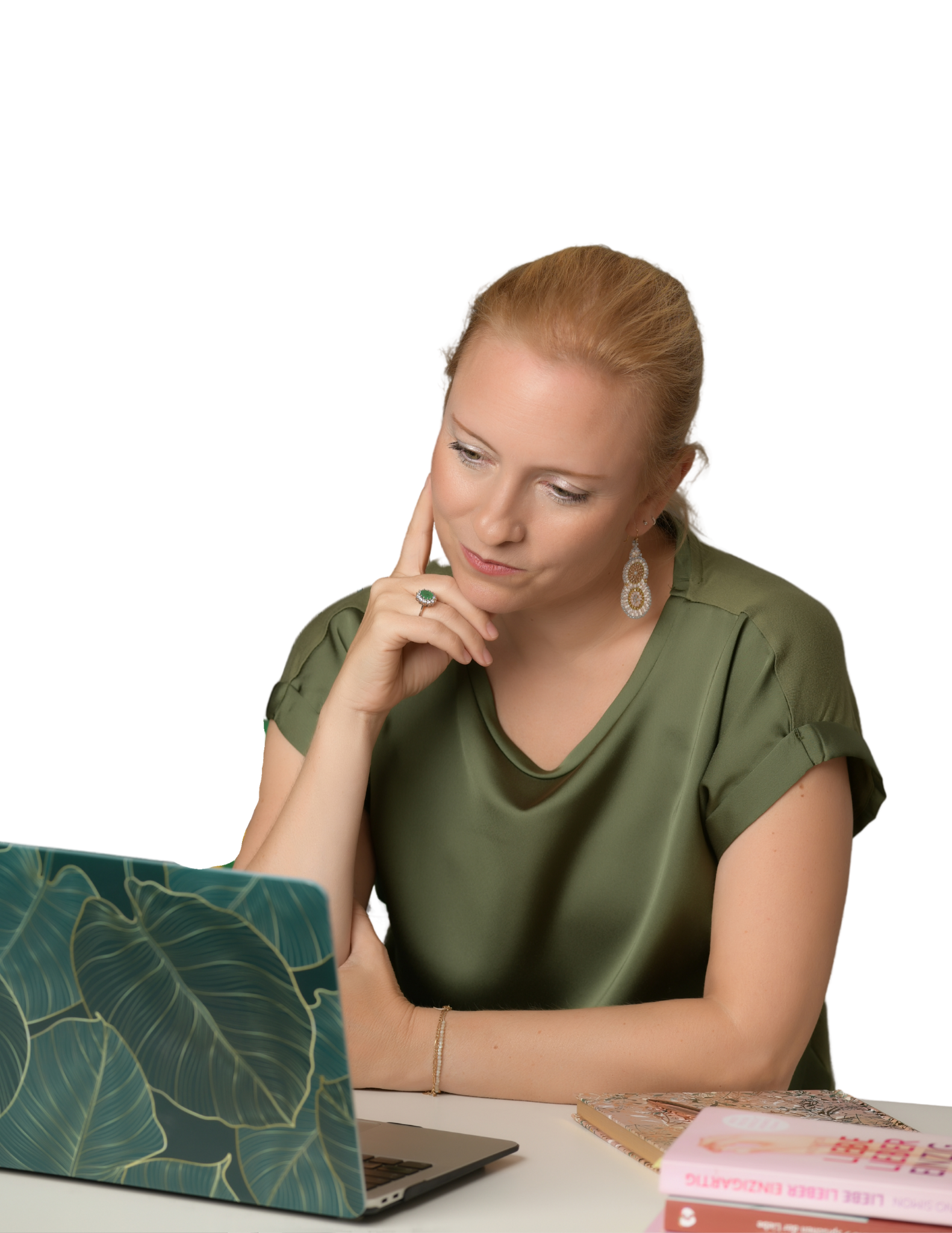 Eine Frau mit blonden Haaren sitzt nachdenklich an einem Tisch, schaut auf einen Laptop mit einem Blätterdruck-Muster. Es liegen Bücher und ein Notizbuch vor ihr.