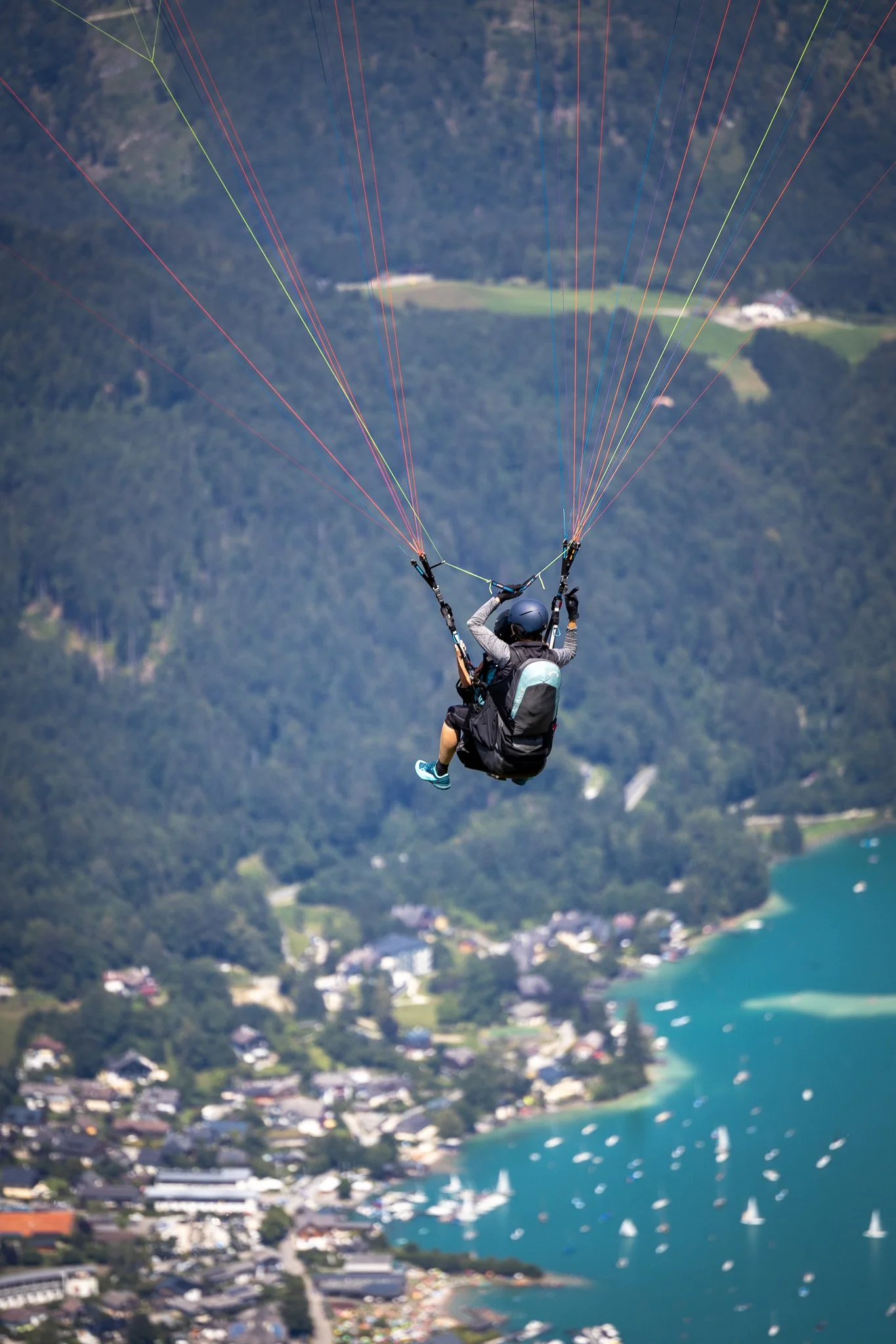 Fallschirmspringer in der Luft über einer Stadt mit Wasser, umgeben von grünen Bergen.