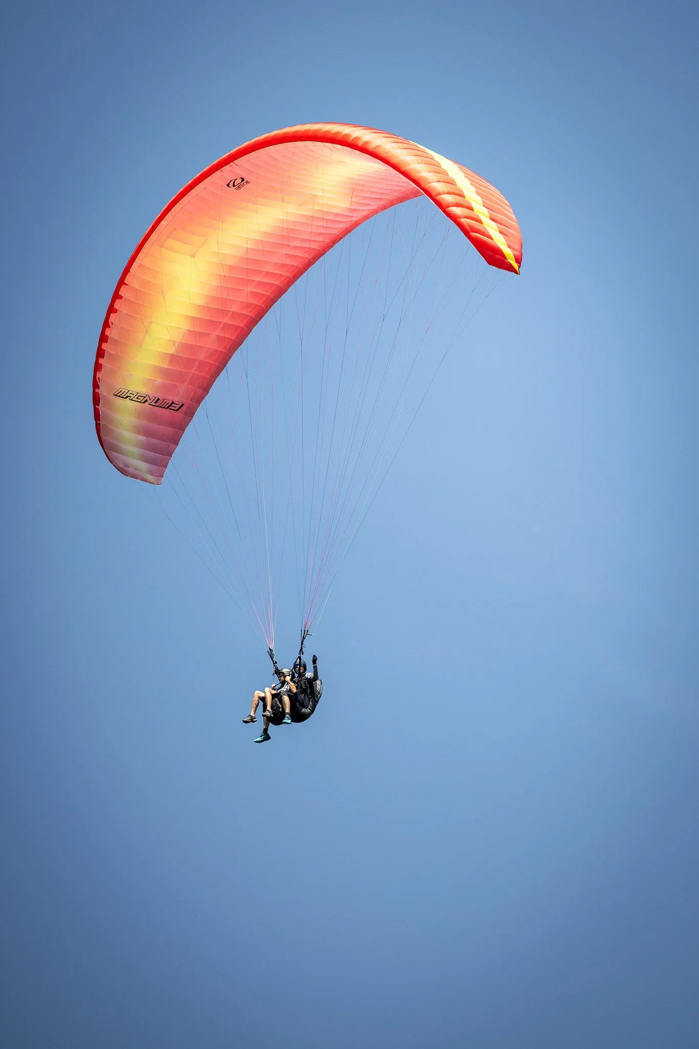 Zwei Menschen beim Paragliding, schwebend in den Himmel mit einer orangefarbenen Gleitschirm, blauer Himmel im Hintergrund.