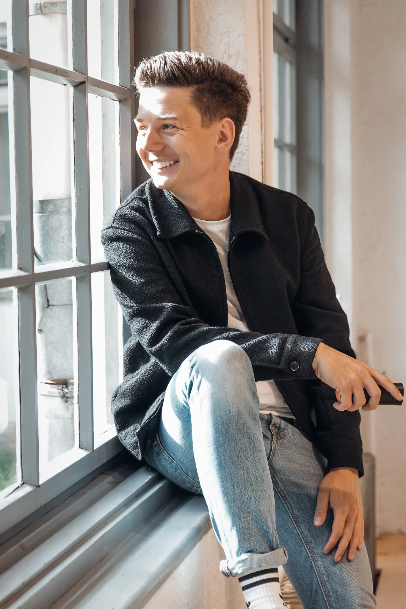 Sebastian Schmidt sitzt lachend am Fenster in einem Raum mit natürlichem Licht.