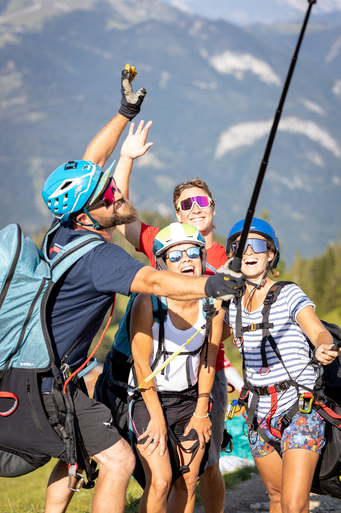 Menschen beim Klettern im Freien, alle tragen Helme und Sonnenbrillen, lachen und posieren für ein Foto gegen eine Bergkulisse.