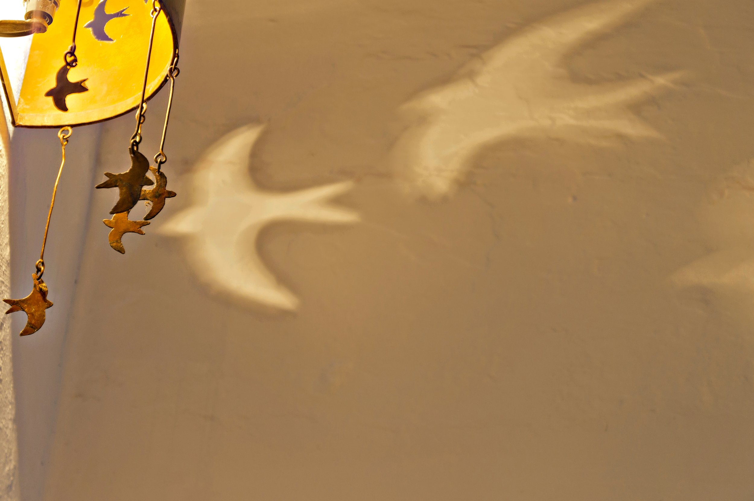 Hanging brass bird decorations casting shadows on a wall.