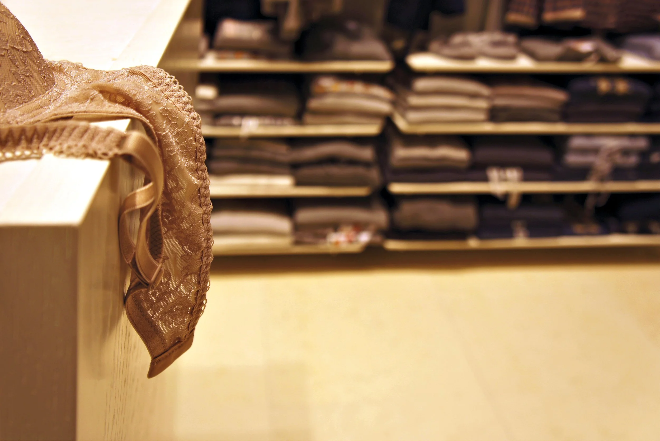 Lace bra displayed on a store counter with folded clothes on shelves in the background.