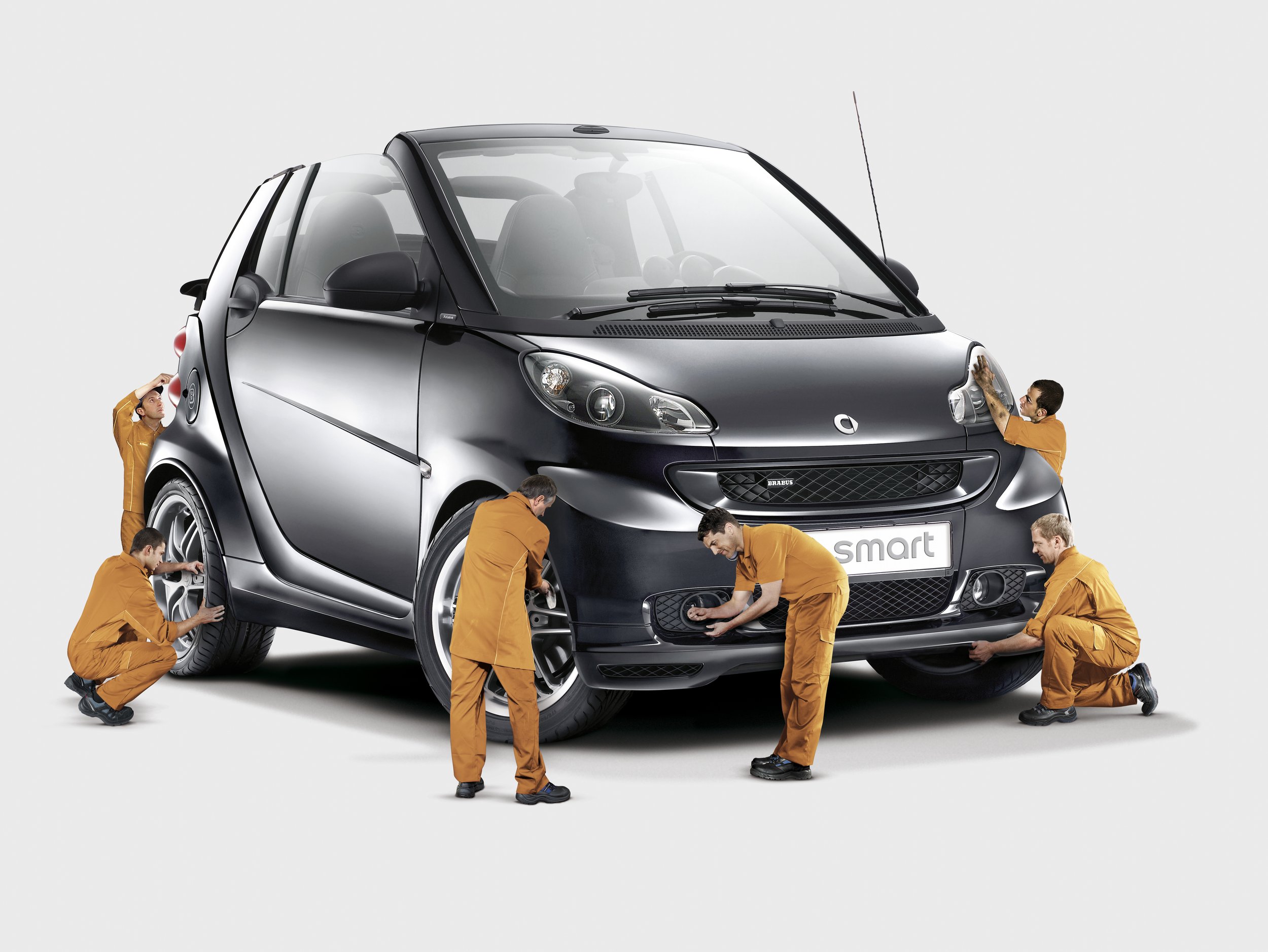 Several people in orange uniforms working on a black Smart car, performing tasks such as polishing and inspecting the vehicle.