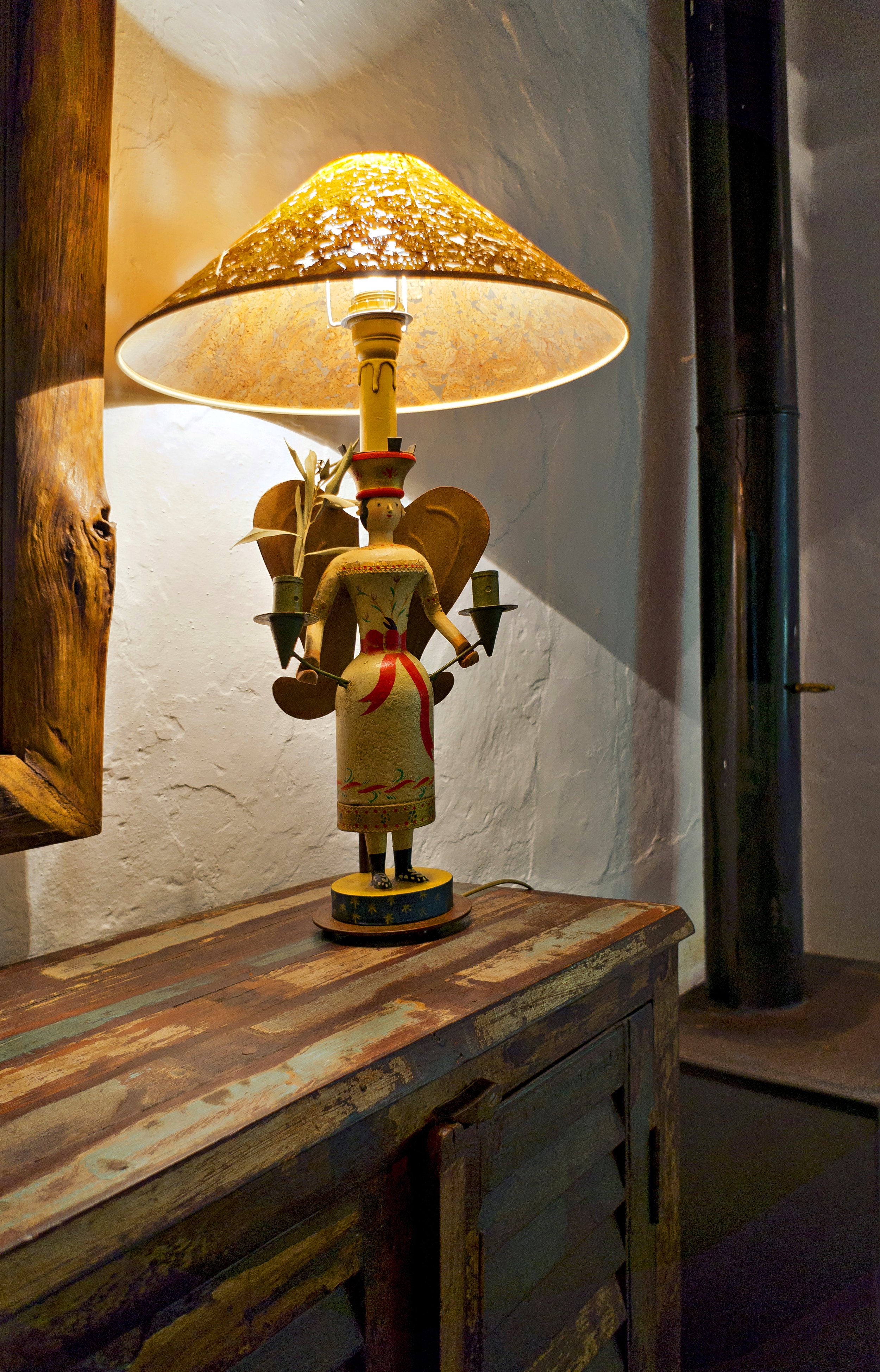 Decorative table lamp with a figure resembling an angel holding candle holders on a rustic wooden table.