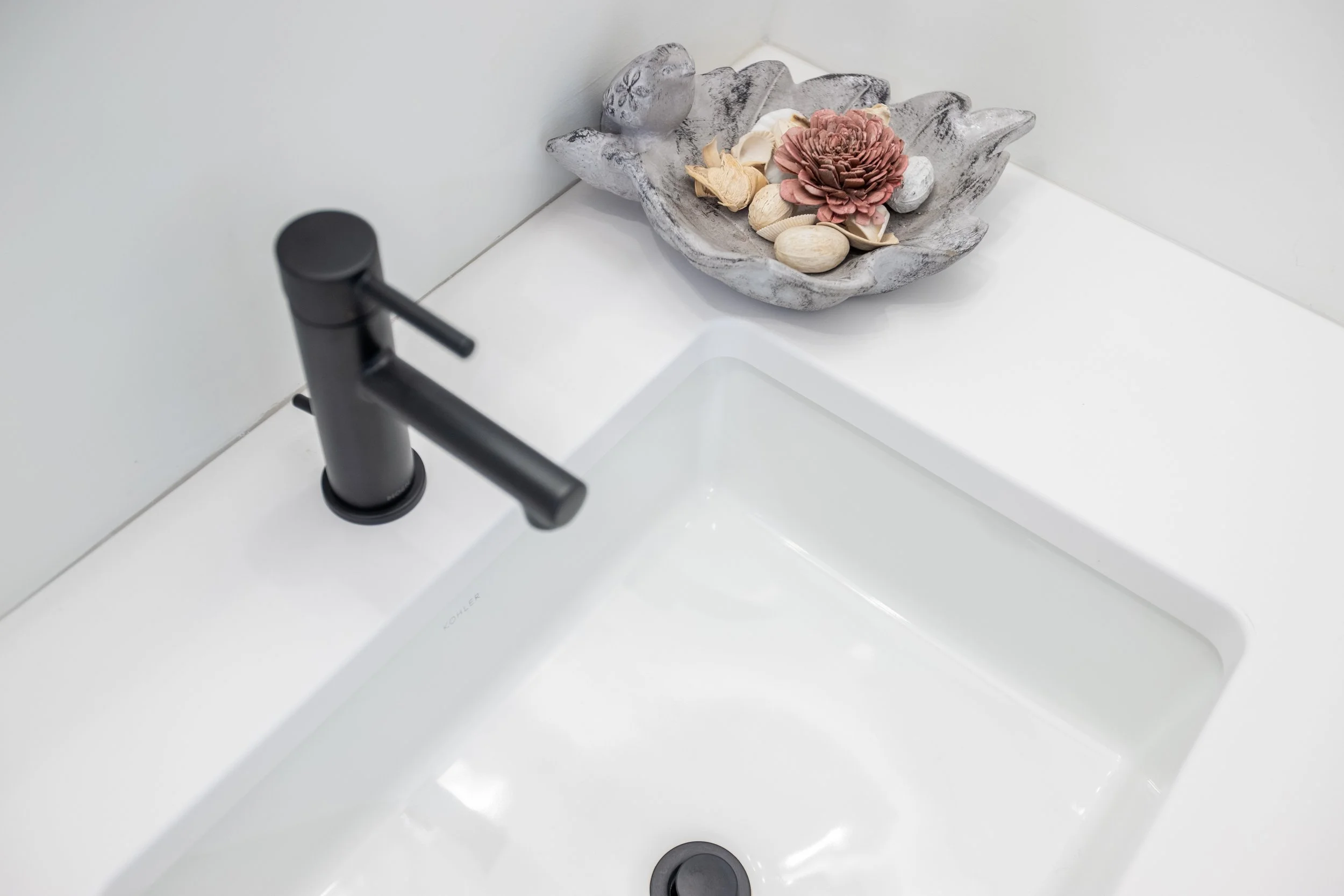 Close-up of a black faucet above a white, quartz sink and countertop.