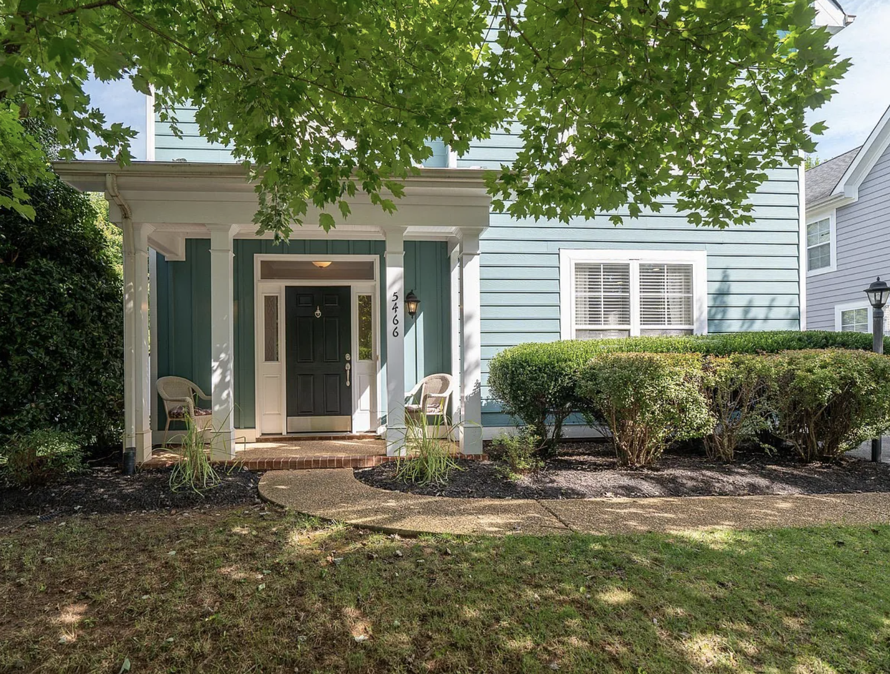 Front porch of a house with teal siding, white trim, and a black door, surrounded by greenery and shrubs, with a concrete walkway leading to the porch. 5466 Park Rd. Crozet, VA.