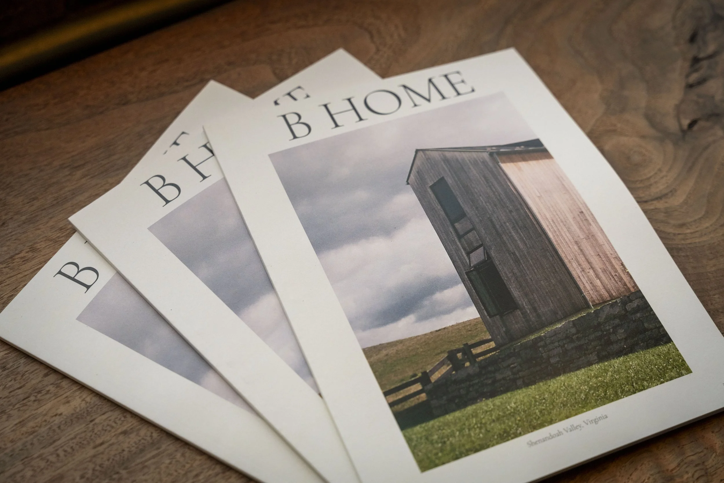 Three magazines with the title 'B HOME' featuring a wooden tiny house on the cover, resting on a wooden surface.
