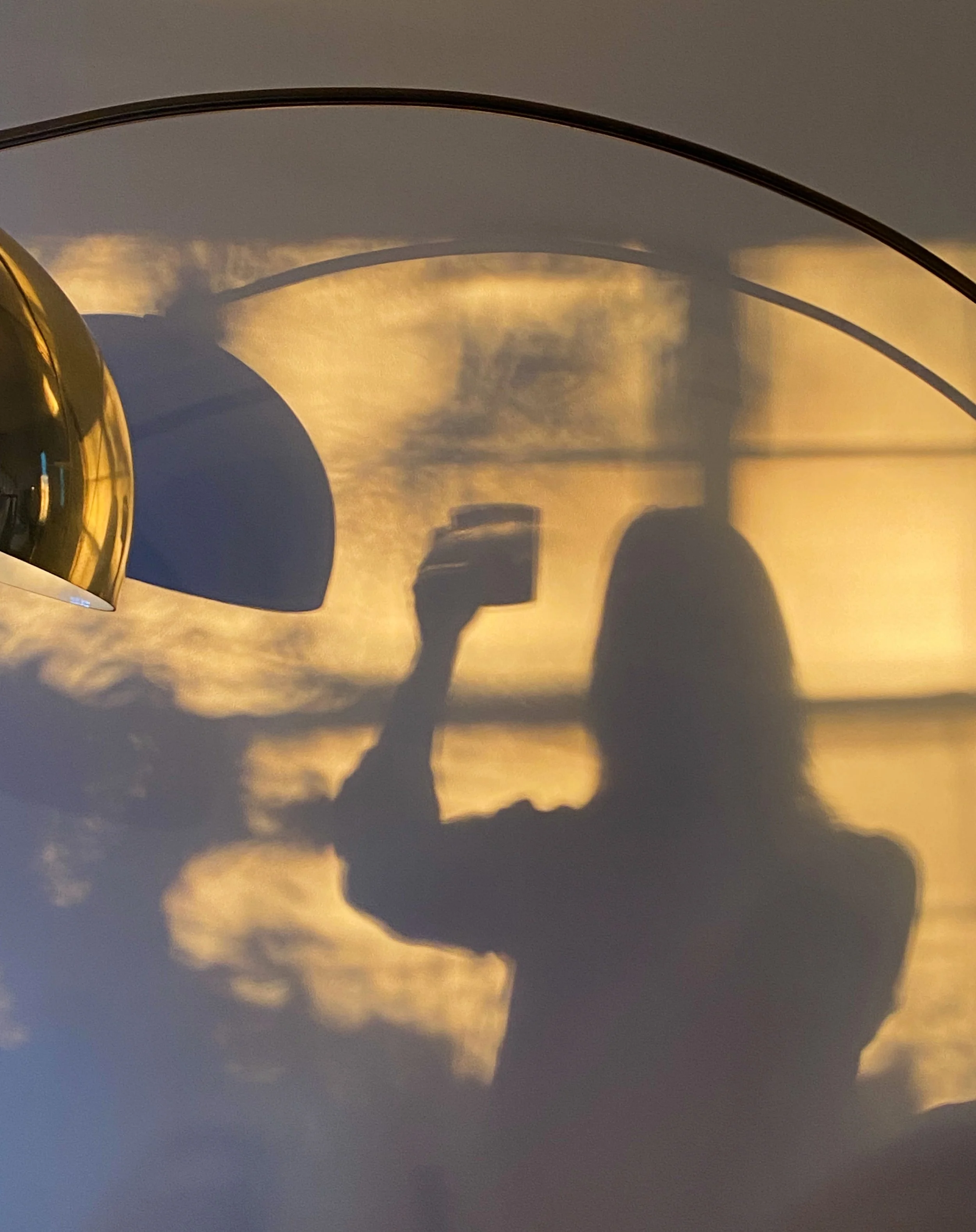 A reflection of a person taking a photo of the sky at sunset, seen on a shiny, curved surface.