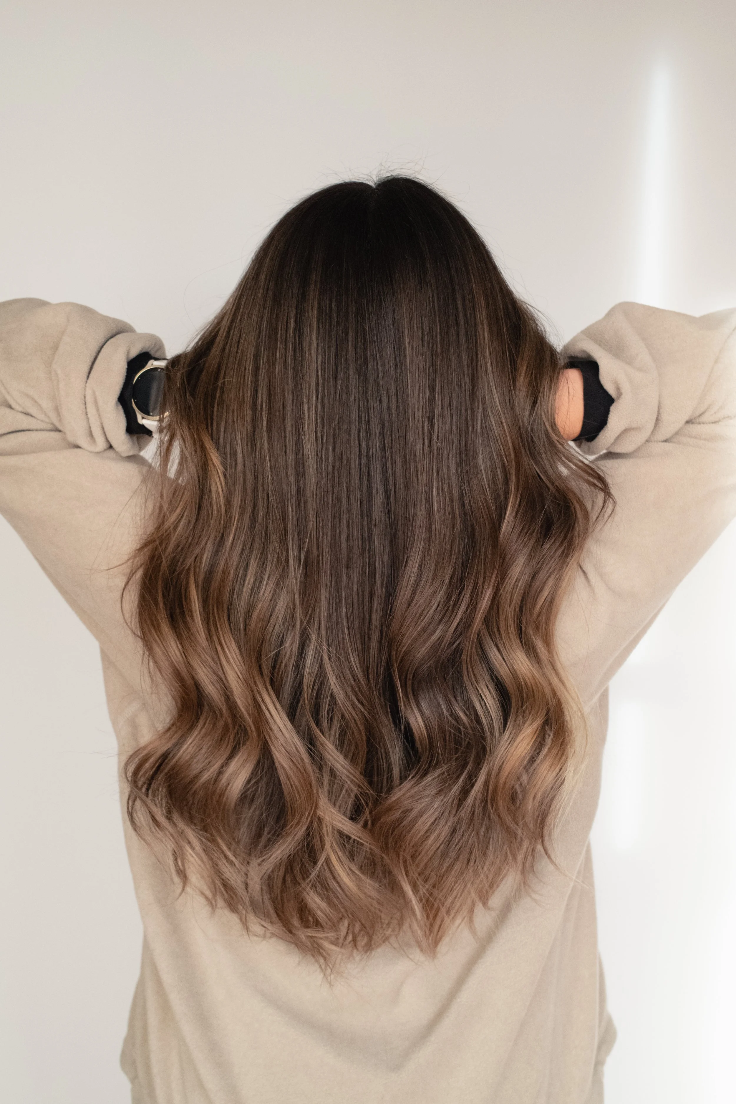 Back view of a woman with long, wavy, ombre hair transitioning from dark brown to light brown.