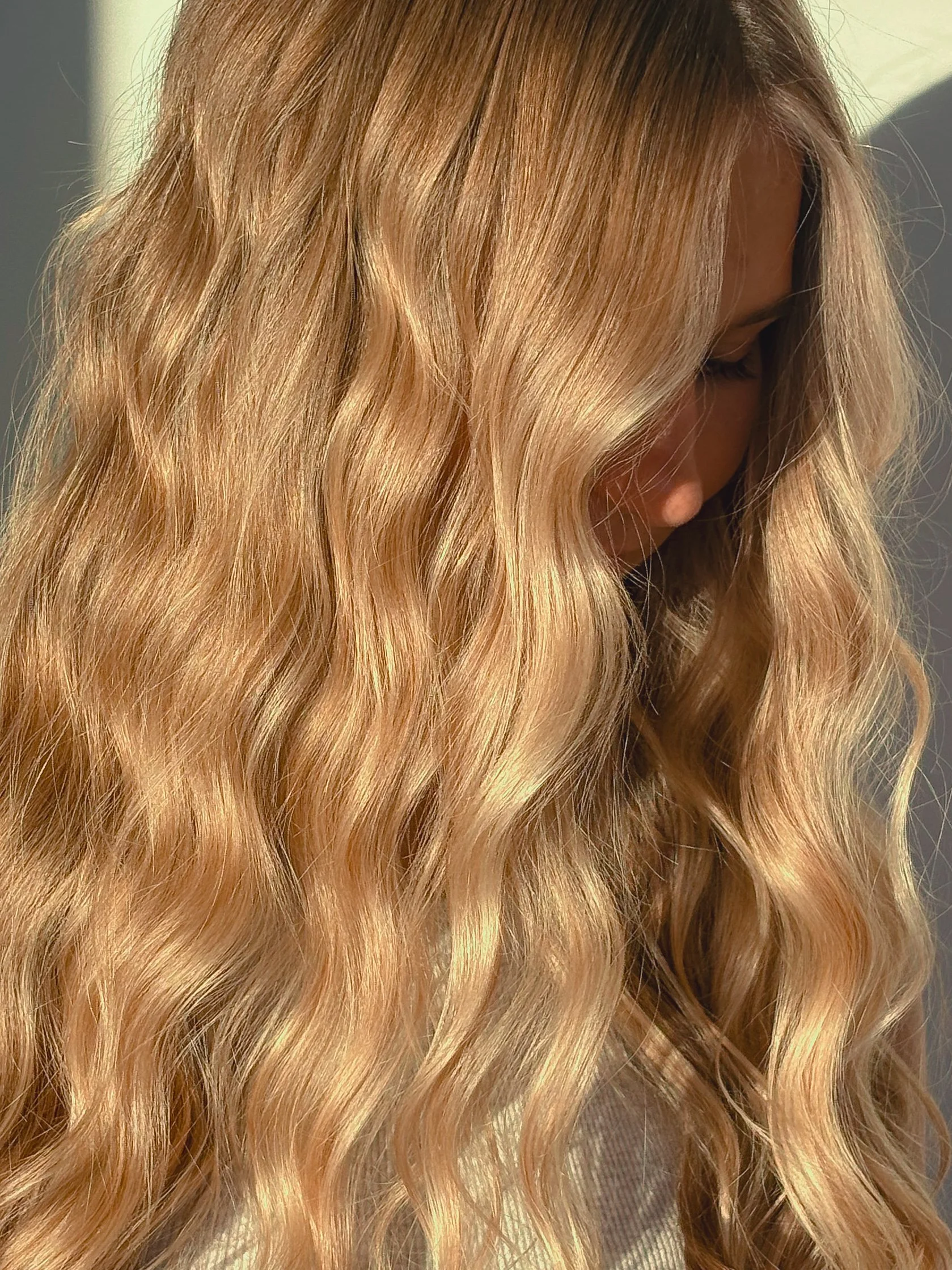 Close-up of a woman with long, wavy, blonde hair looking downward with her eyes closed.