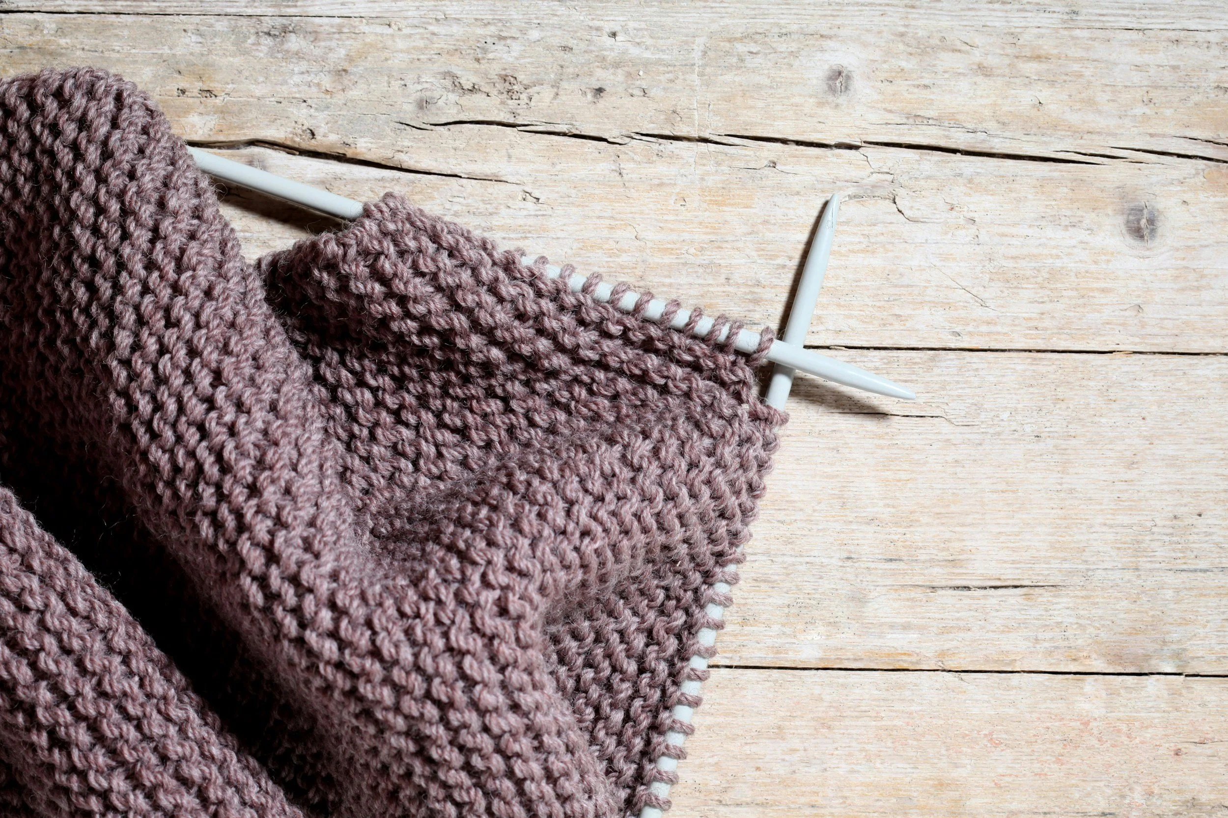 Pink knitting yarn on a knitting needle on a wooden surface.