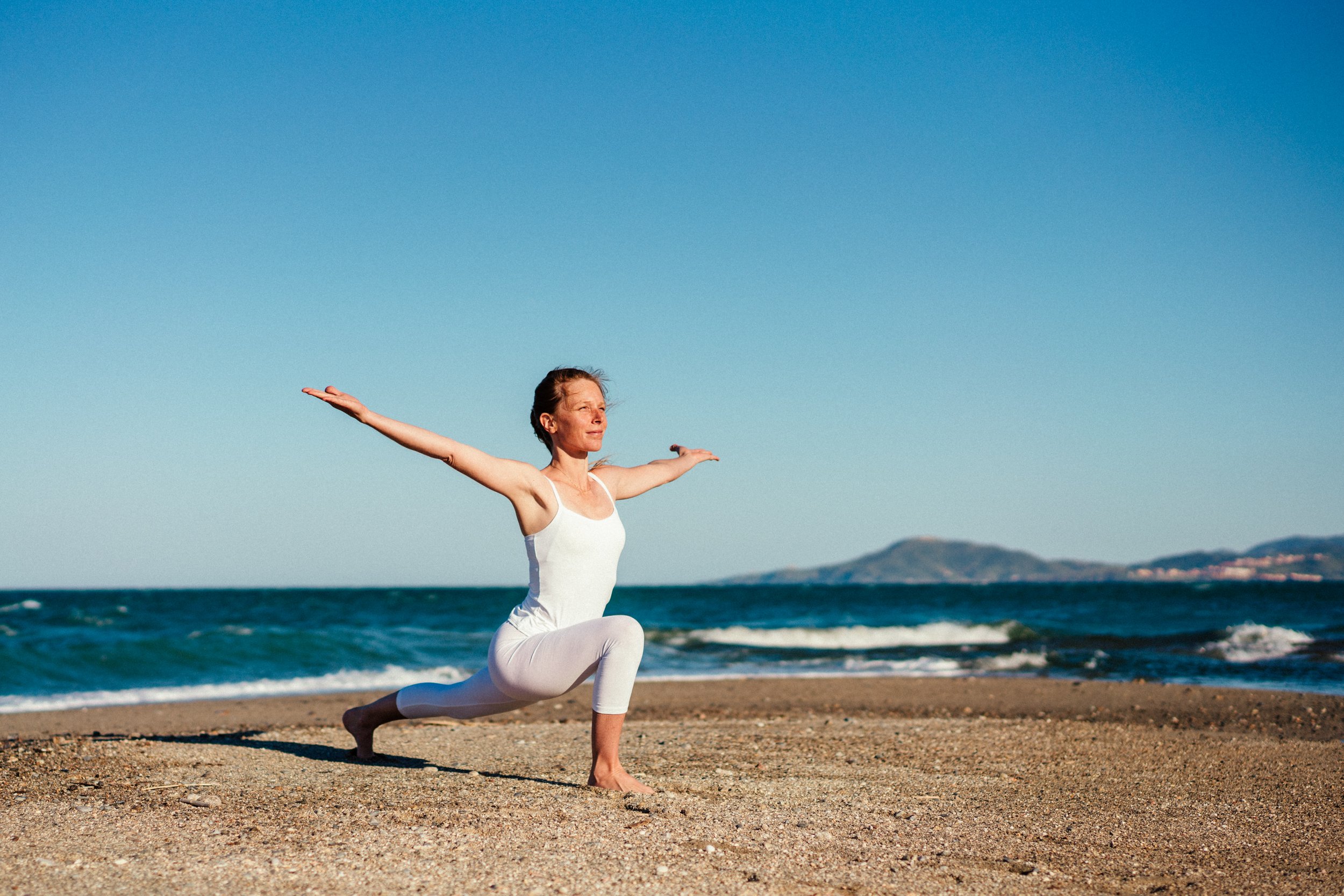 iris chasles professeur de yoga en posture du guerrier sur la plage