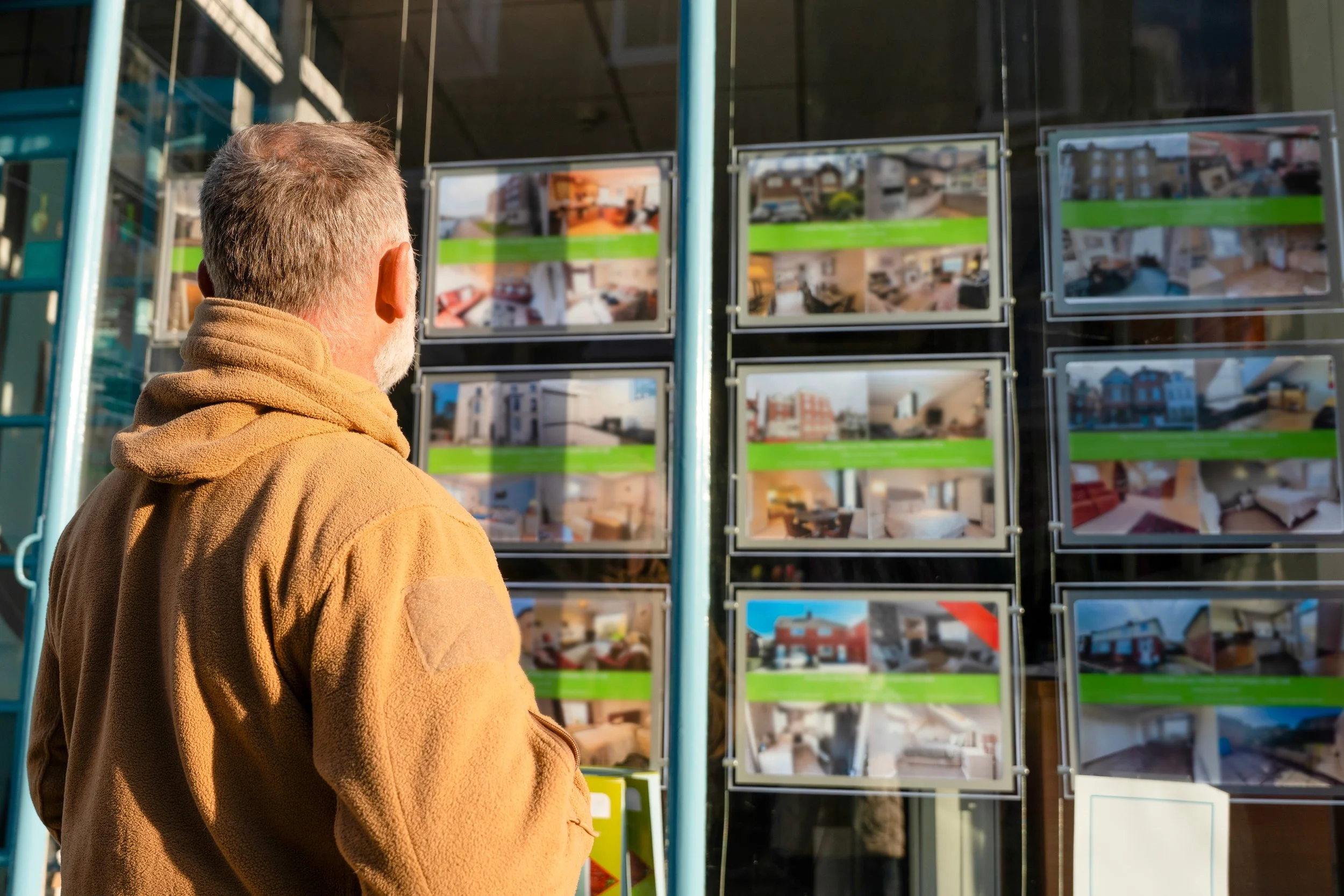 A prospective home buyer reviewing local real estate listings displayed in a shop window.