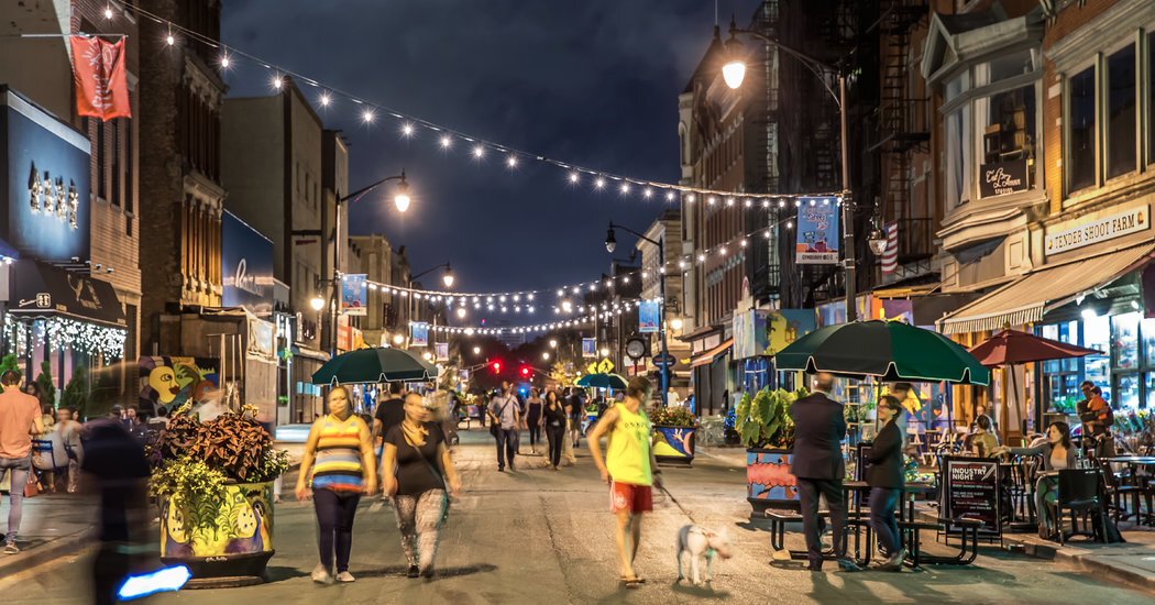 People walking and dining outdoors along a well-lit pedestrian street lined with shops and overhead string lights at night.