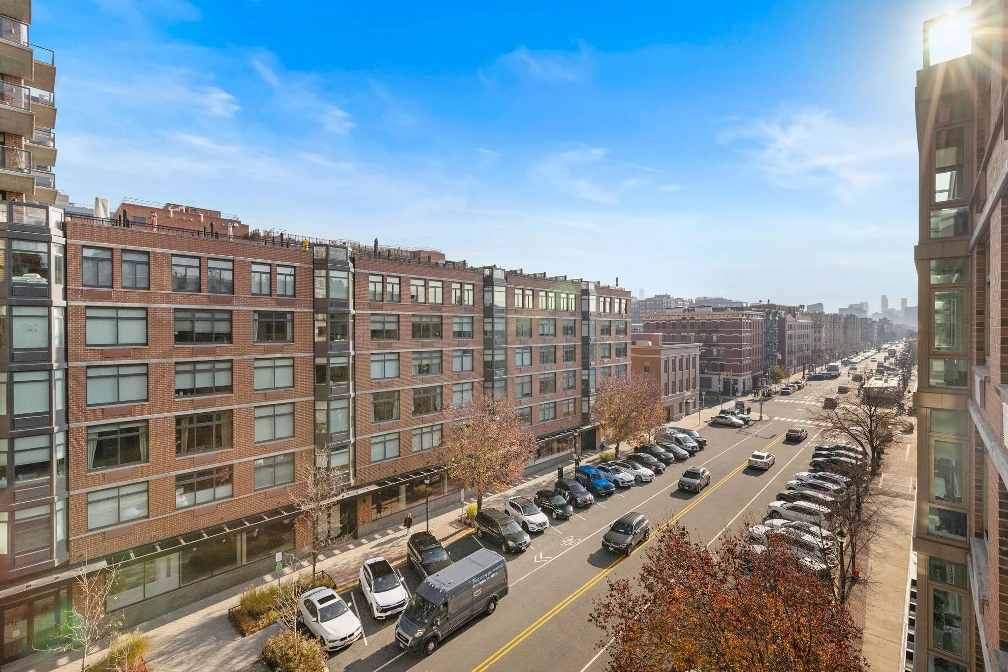 Aerial street view of a Hudson County NJ residential neighborhood showing mid-rise brick apartment buildings and parked cars on a sunny day