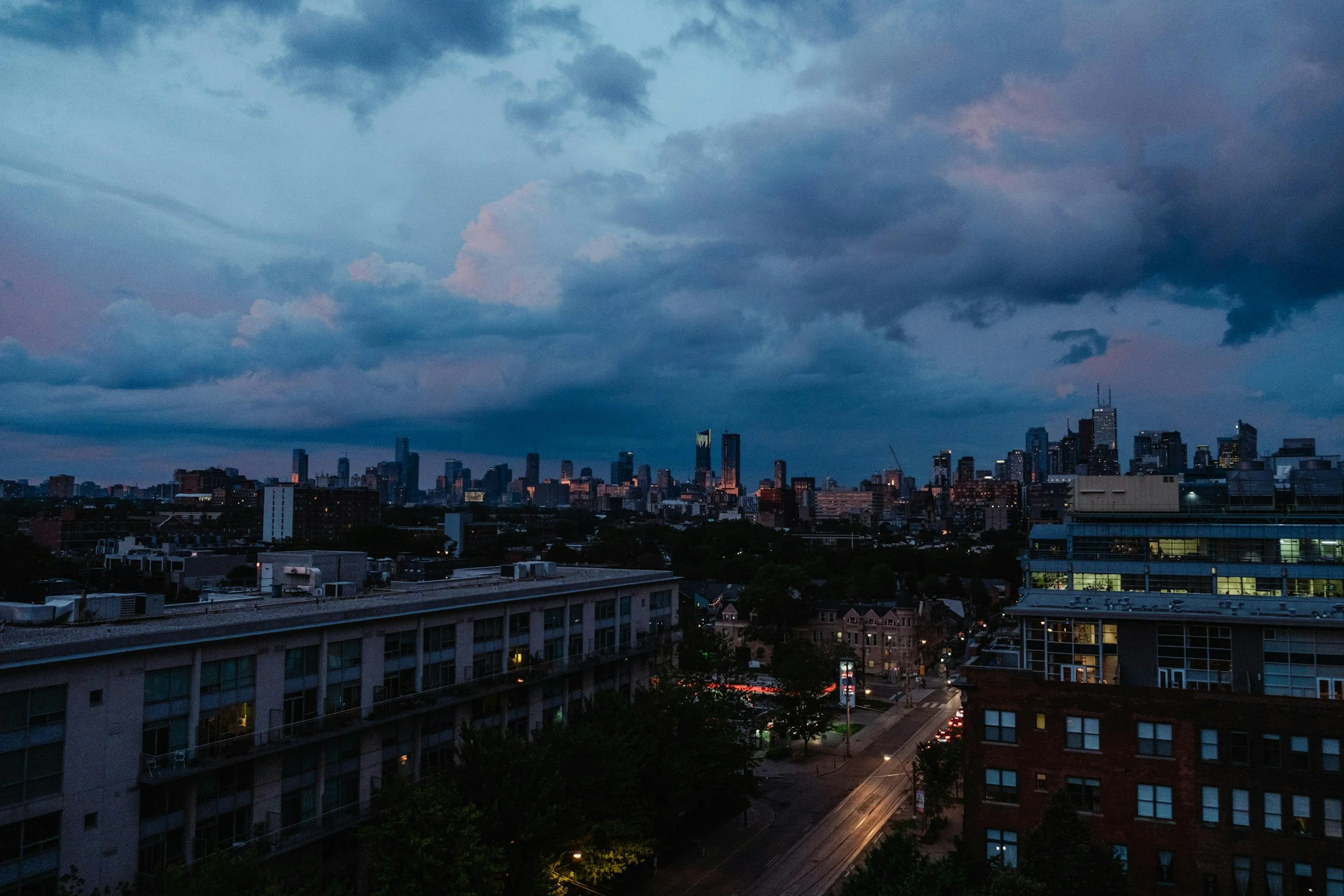 Elevated view of Jersey City residential buildings and streetscapes under a dramatic twilight sky with city buildings in the distance.