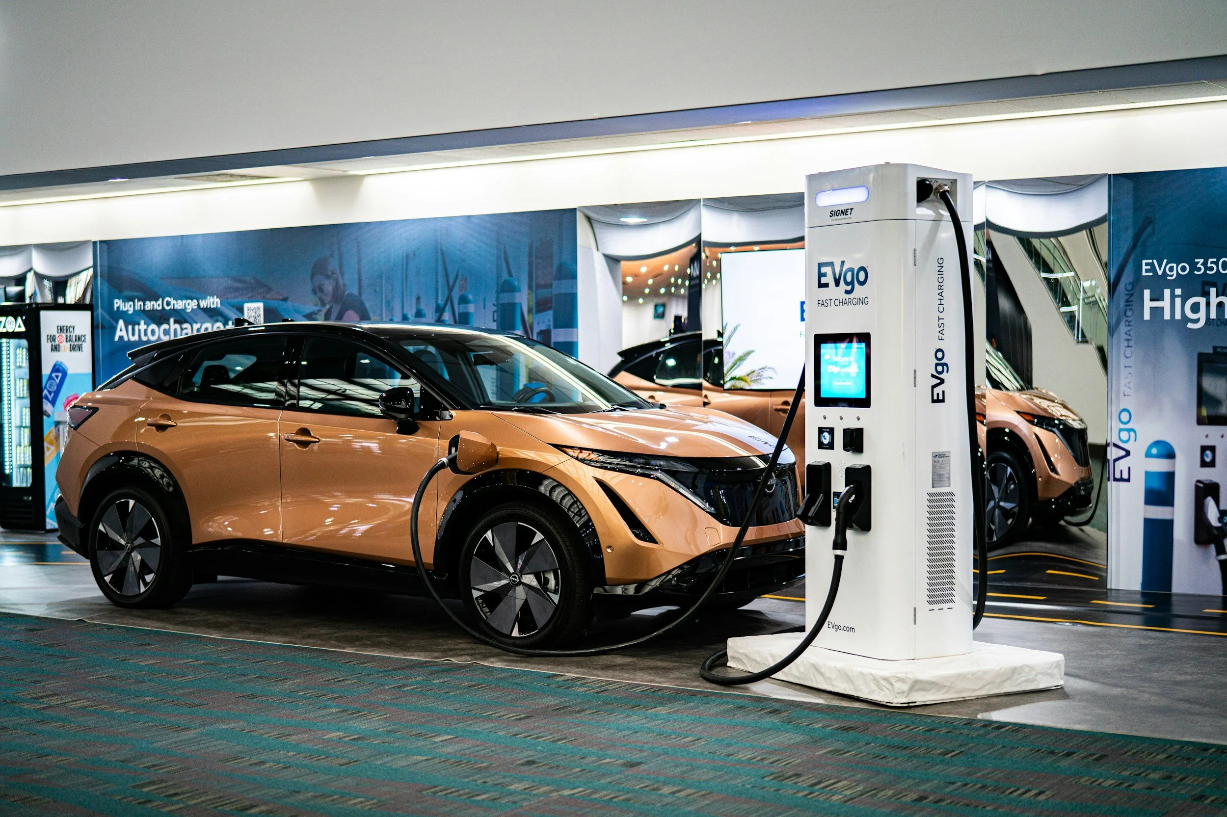 A copper electric SUV plugged into a white EVgo fast charging station inside a parking facility.