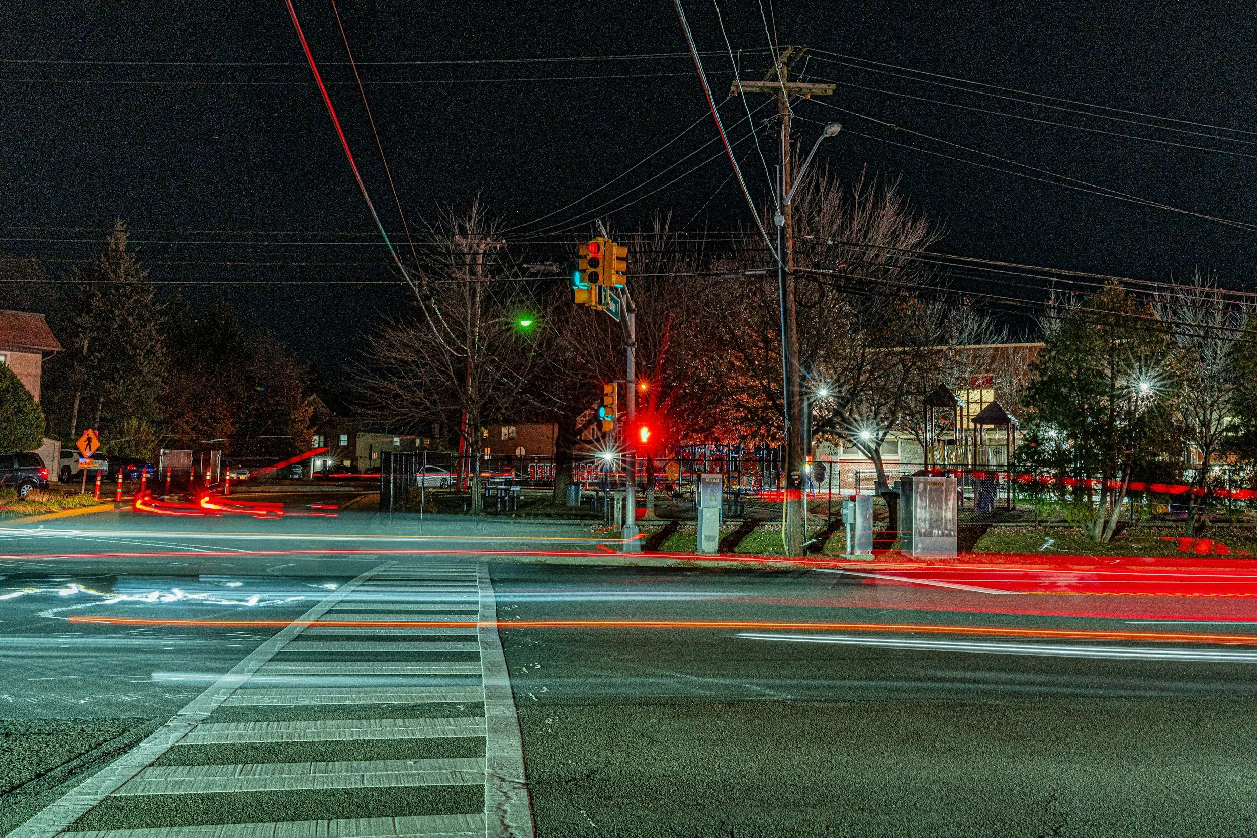 Long exposure photograph of a well-lit urban intersection at night with red traffic lights and light trails from passing cars.