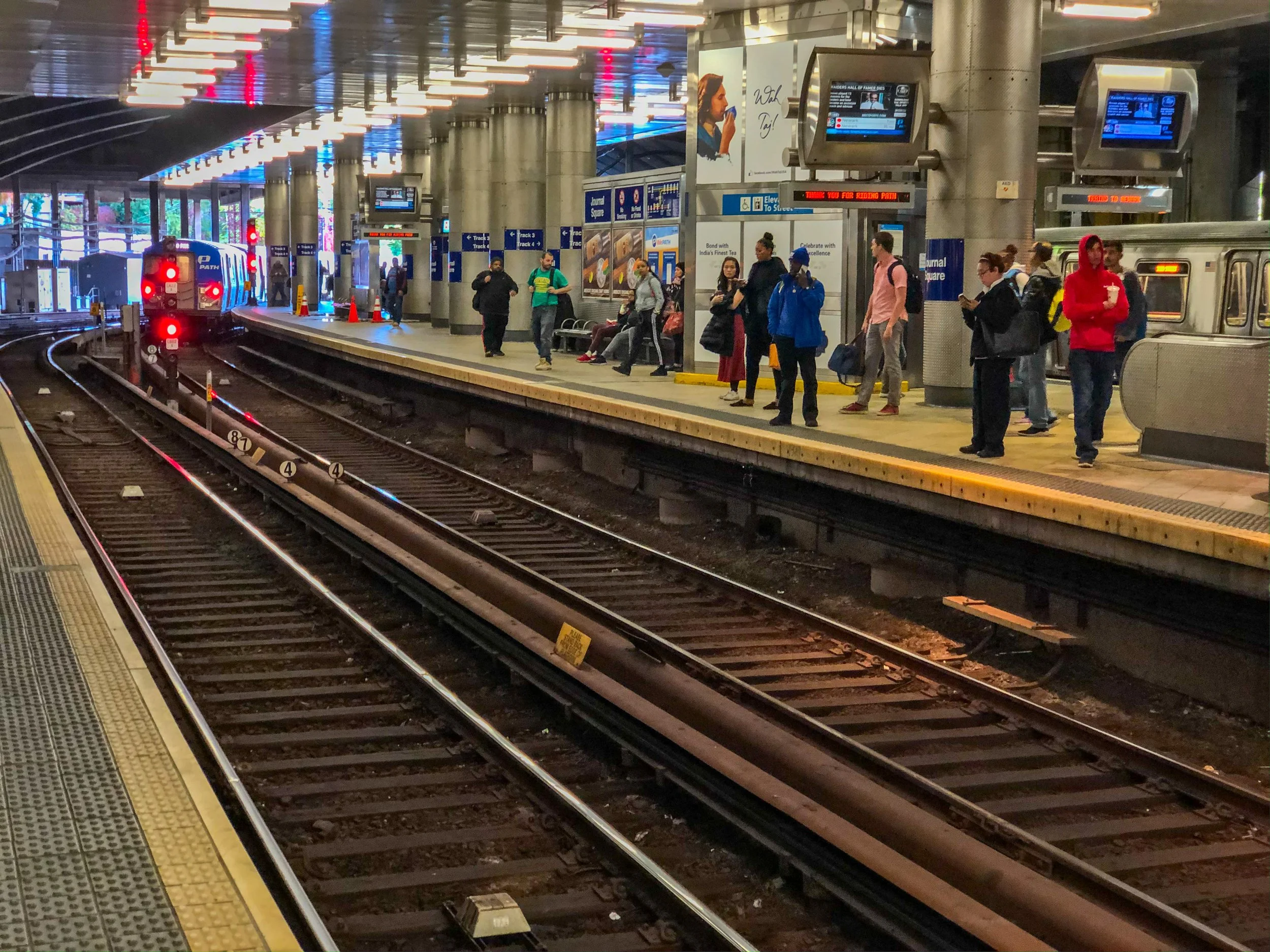 Passengers waiting on the train platform at the Journal Square PATH station in Jersey City as a train approaches on the tracks.