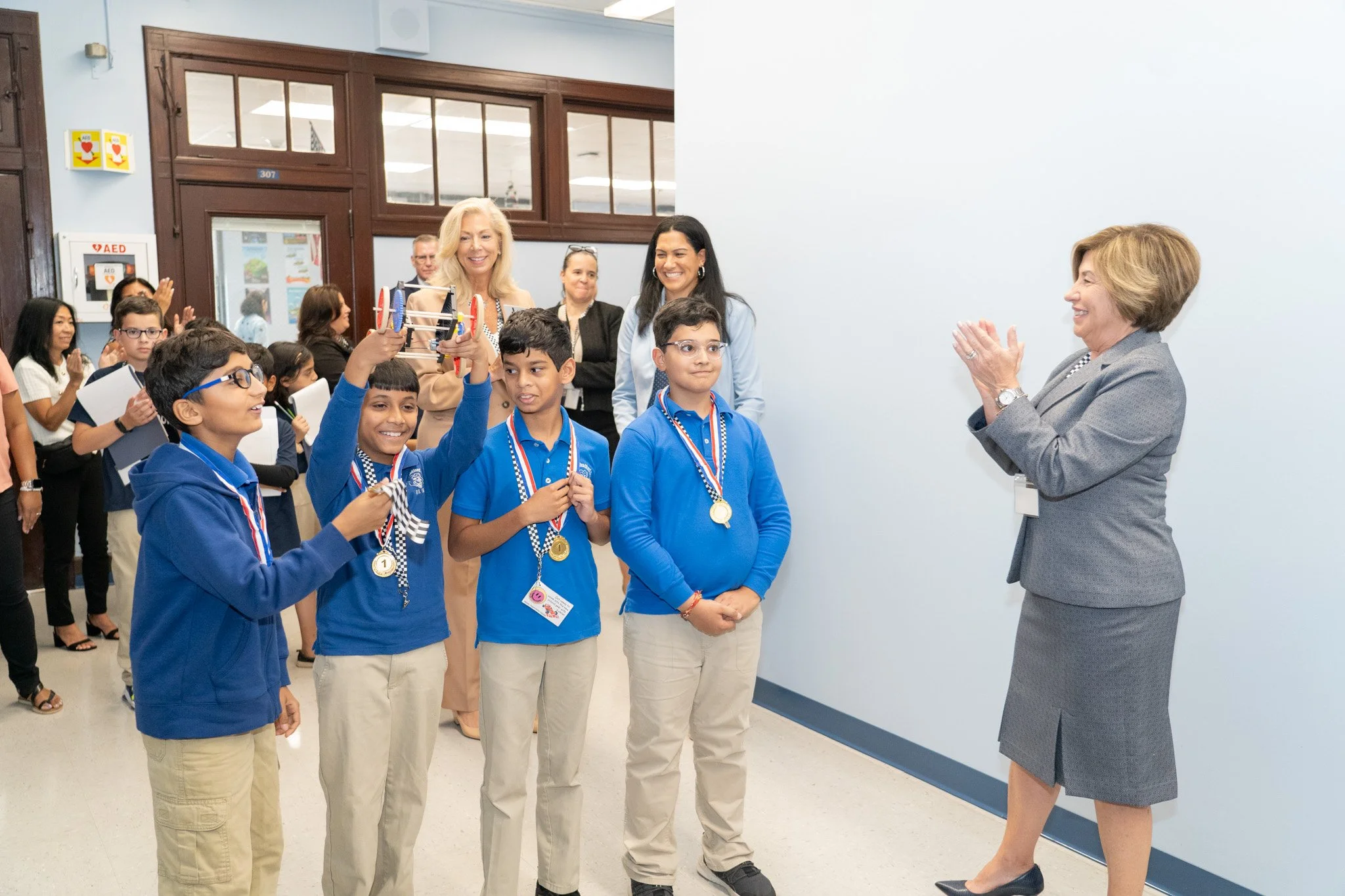 Smiling Jersey City NJ students with awards around their necks, the faculty is smiling and clapping in congratulations