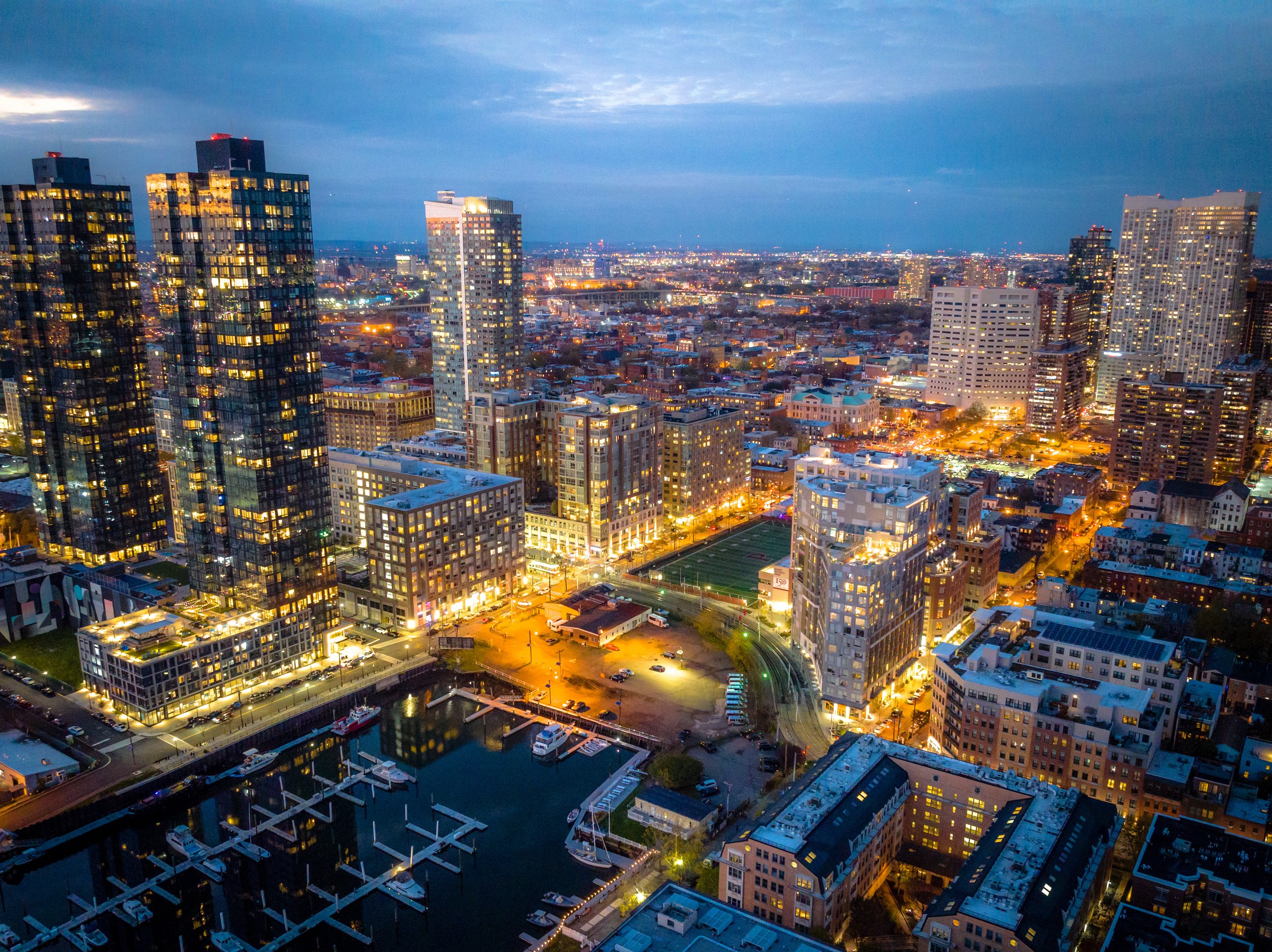 An illuminated aerial view of high-rise condo buildings and a marina at night in a dense urban neighborhood.