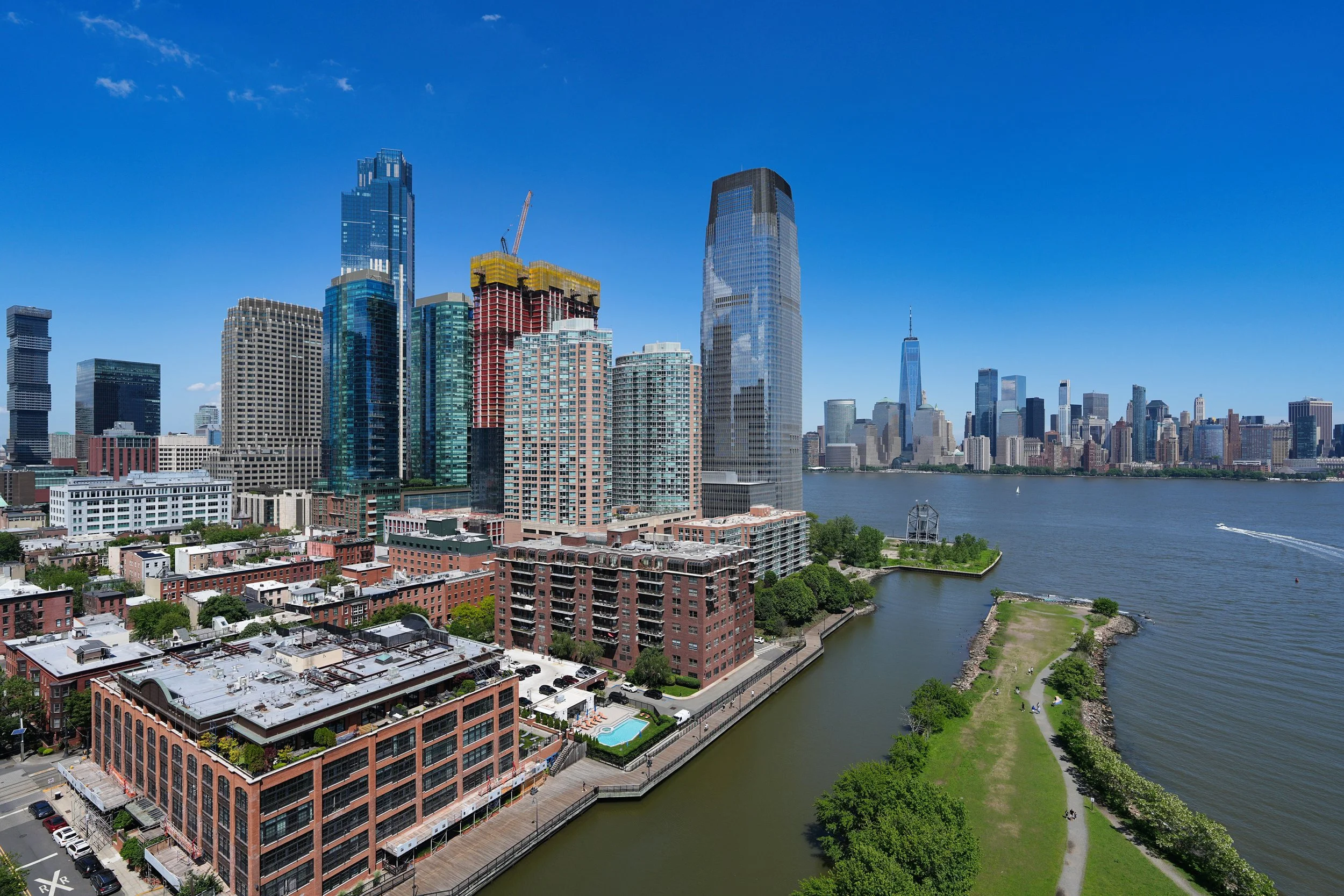 Aerial view of the Jersey City waterfront skyline along the Hudson River featuring modern residential high-rises and waterfront parks.