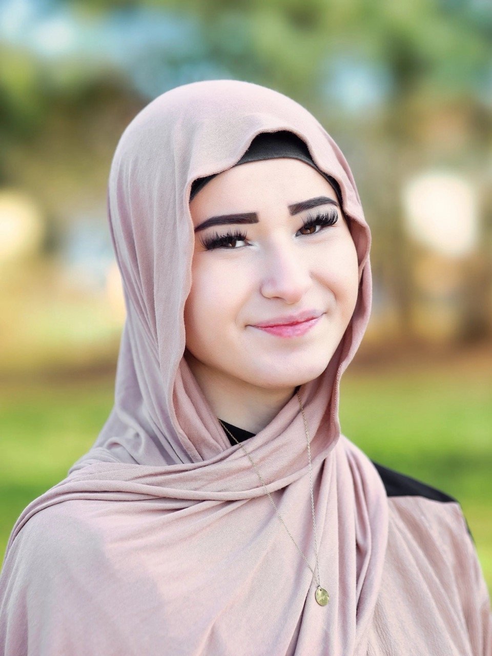 Porträt einer Frau mit rosa Hijab, die in die Kamera lächelt, im Freien bei natürlichem Licht.