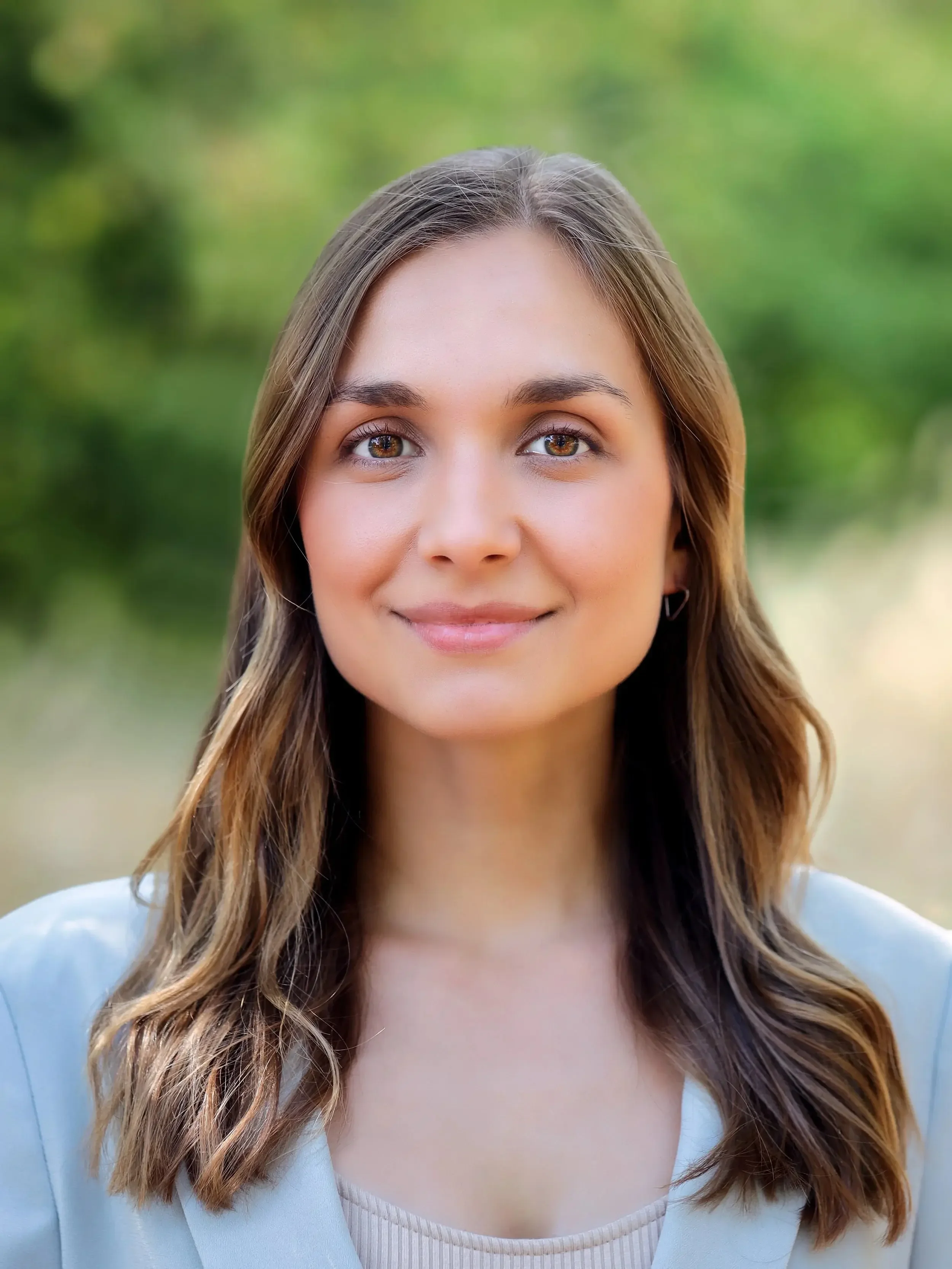 Nahaufnahme einer lachenden jungen Frau mit braunen, gewellten Haaren vor einem grünen, unscharfen Hintergrund.