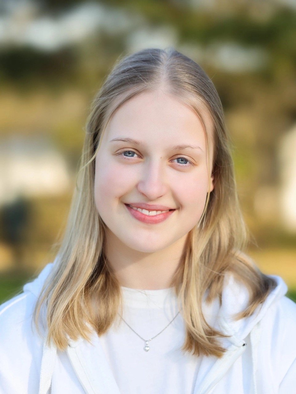 Porträt einer lächelnden jungen Frau mit blonden Haaren und einem weißen Oberteil.