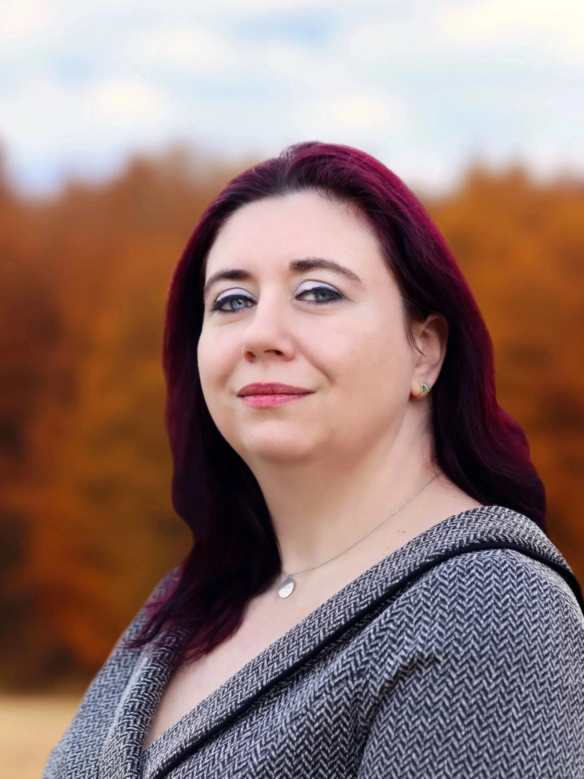 Frau mit dunklem roten Haar und blauen Augen vor herbstlichem Hintergrund