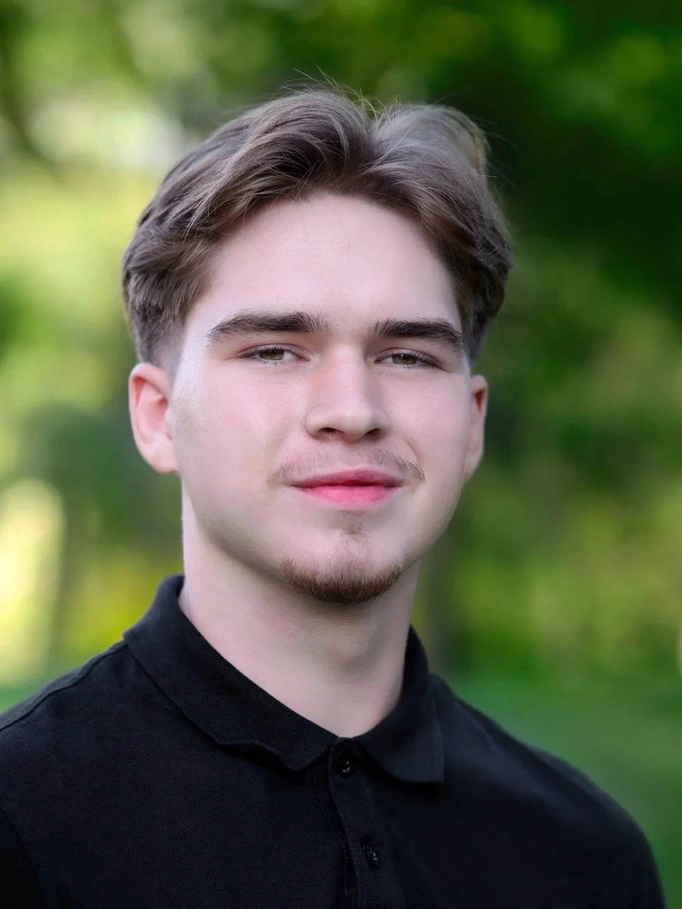 Porträt eines jungen Mannes im Freien mit unscharfem grünem Hintergrund.