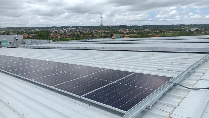 Rooftop solar panels under a cloudy sky, overlooking a distant town and landscape.