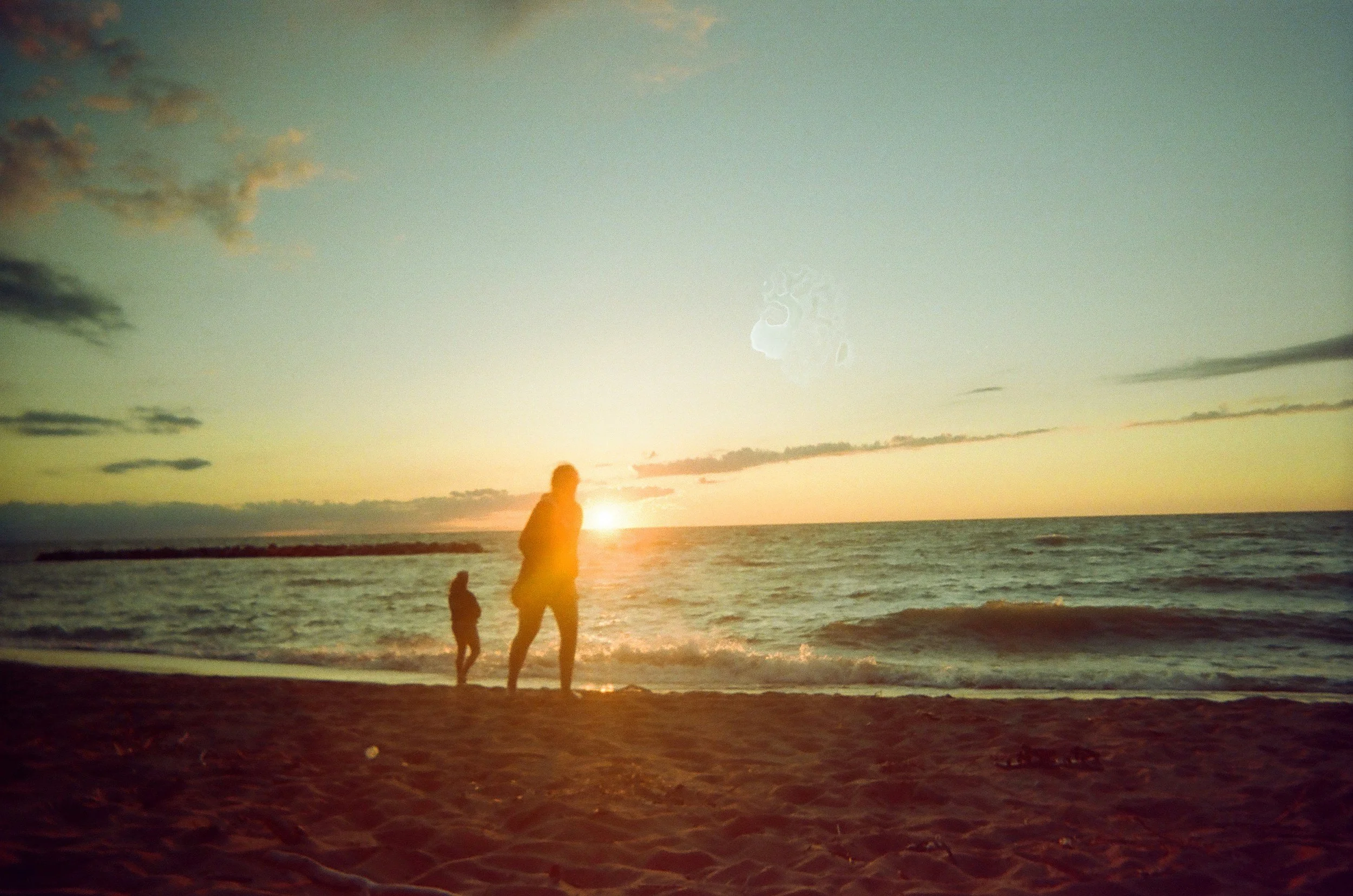 Figures walking along the shoreline at dusk, representing transition and related leadership pathways